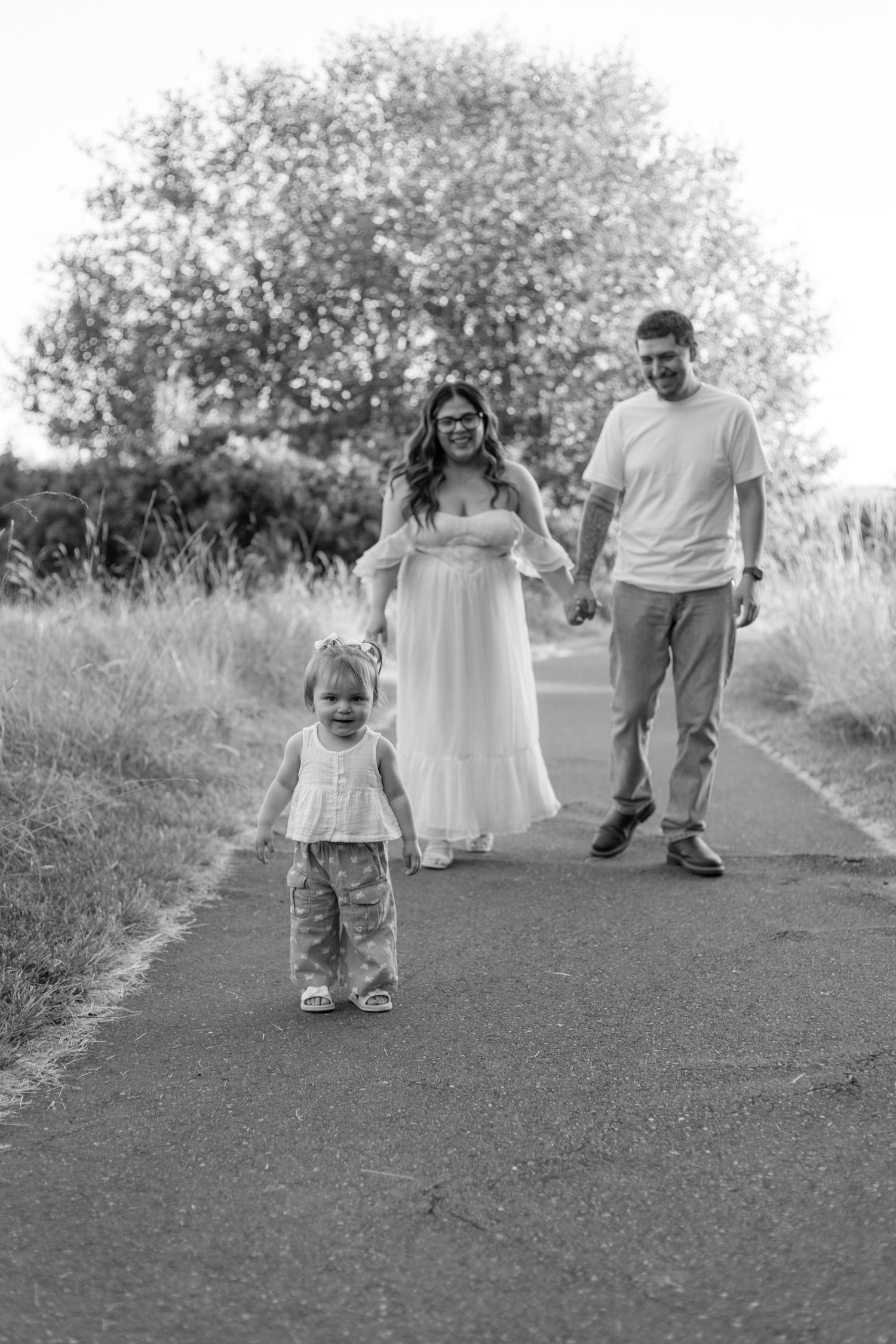 Black and white photo of a family walking together on a path surrounded by tall grass and trees.