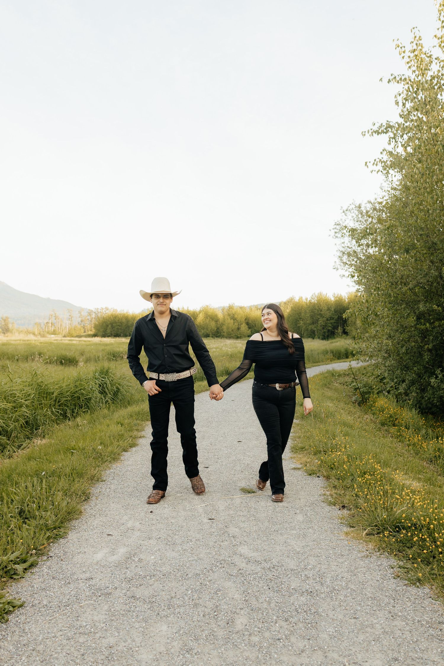 Two people walk together holding hands on a gravel path surrounded by autumn foliage in golden sunlight.