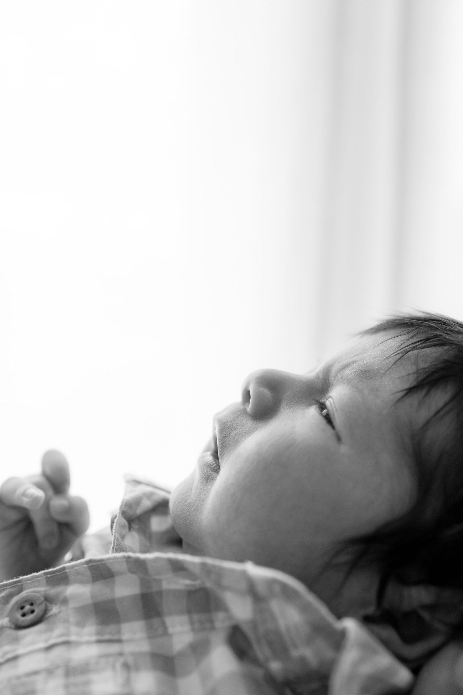 A baby in a plaid shirt lies peacefully sleeping in black and white photography.