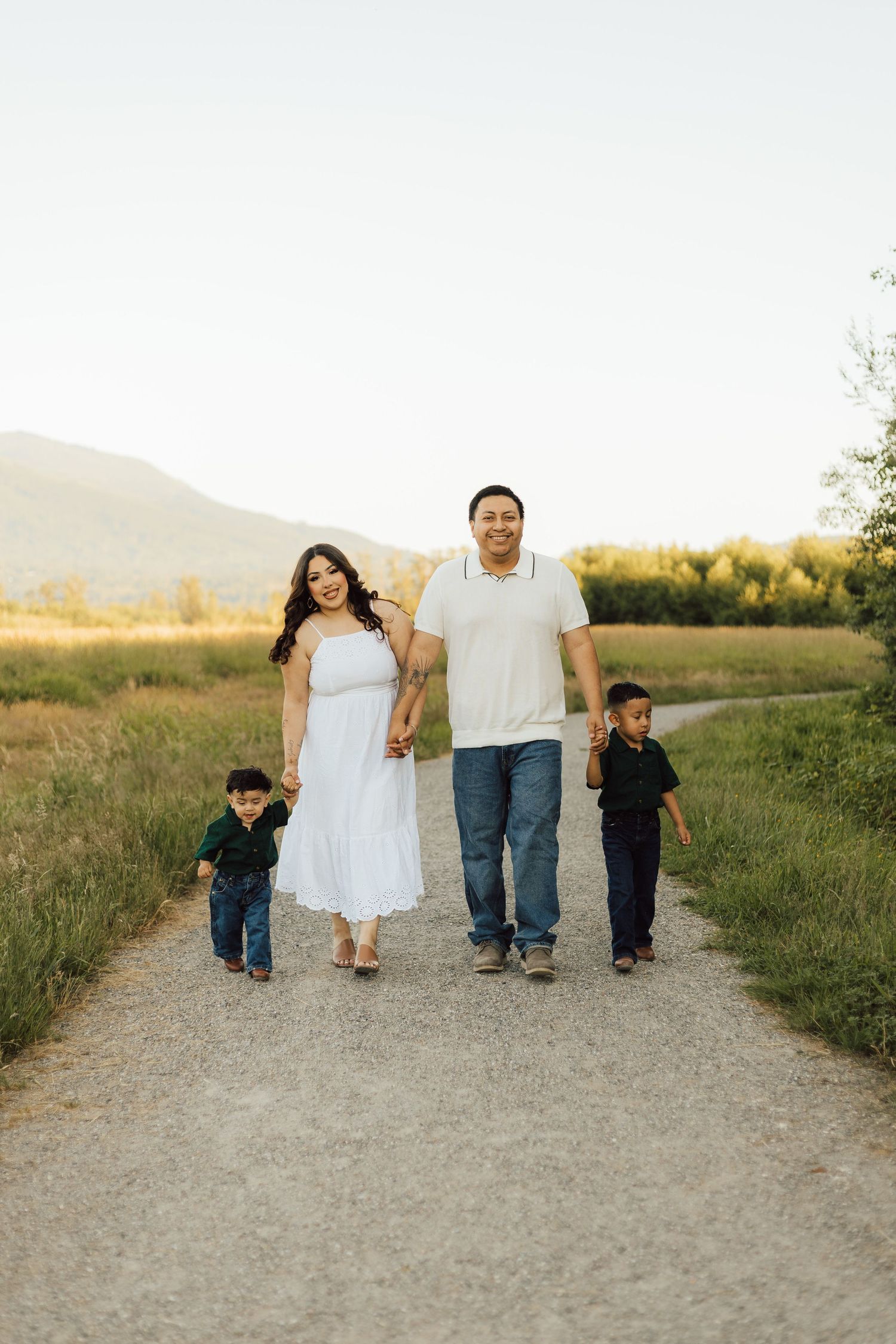 Family walking together on a dirt trail through grassy fields at sunset.