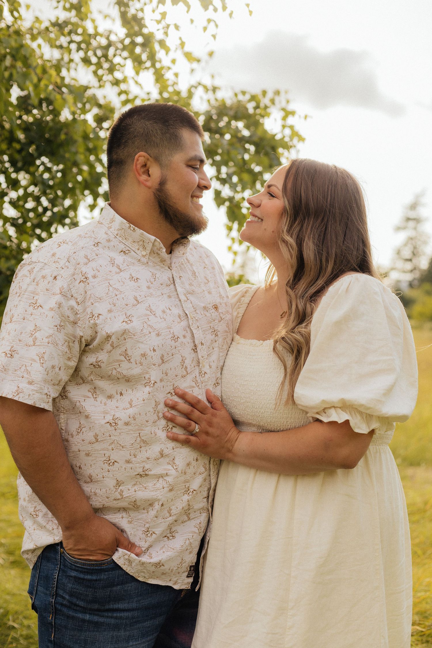 A couple in casual attire embraces and laughs together during a romantic outdoor photoshoot at golden hour.