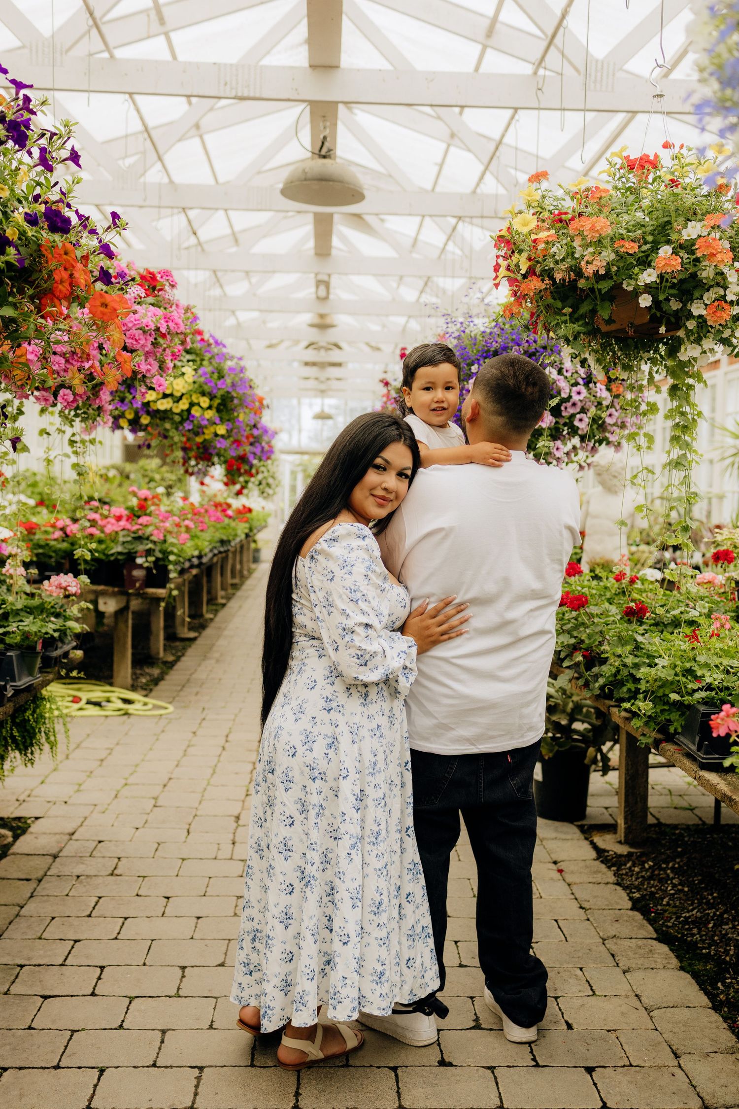 A family shares an intimate moment together in a greenhouse filled with vibrant hanging flower baskets and colorful blooms.