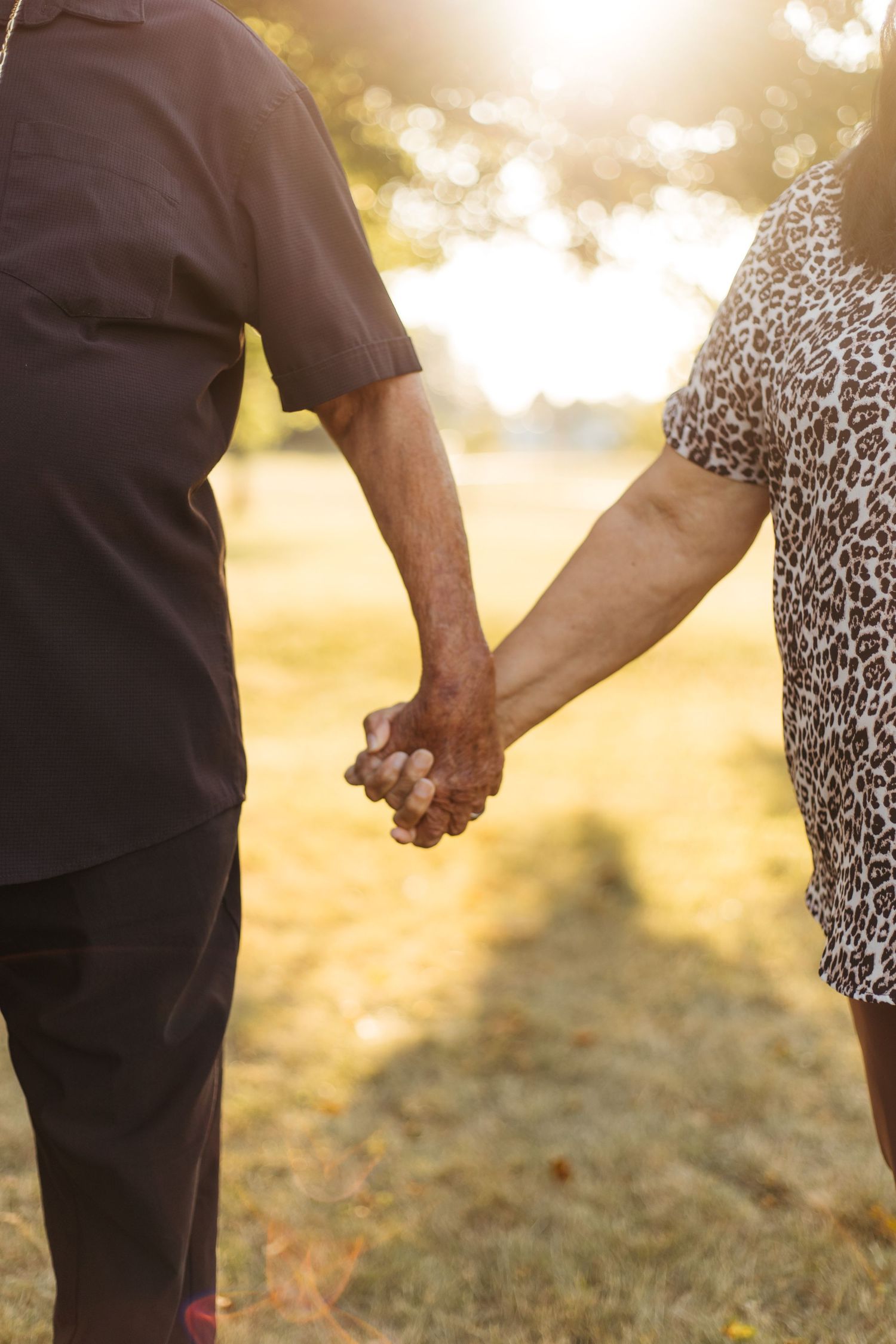 Close-up view of a couple holding hands against golden sunlit background outdoors.
