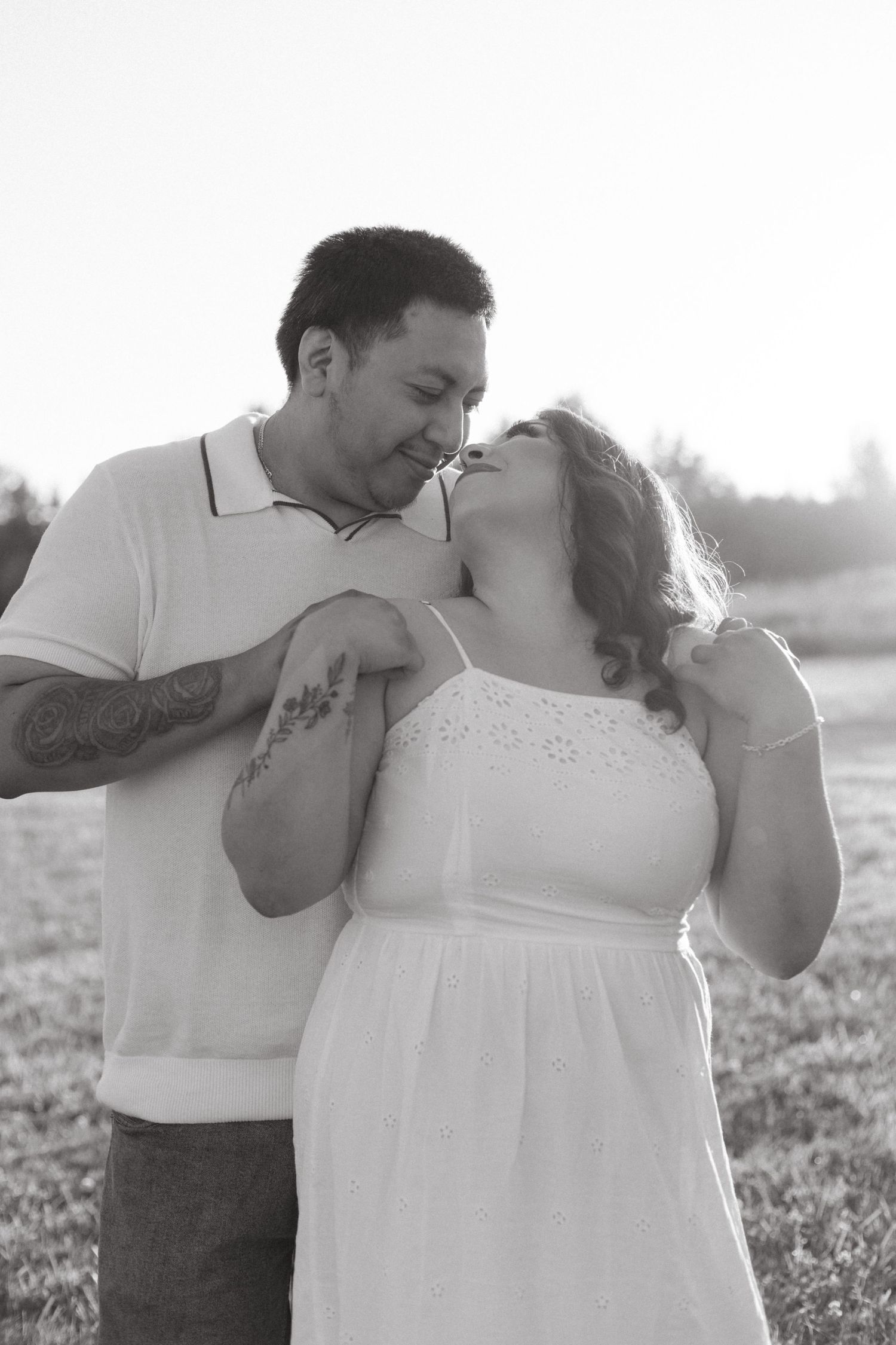 A couple shares a tender moment together outdoors, with sunlight creating a soft backlit glow behind them.