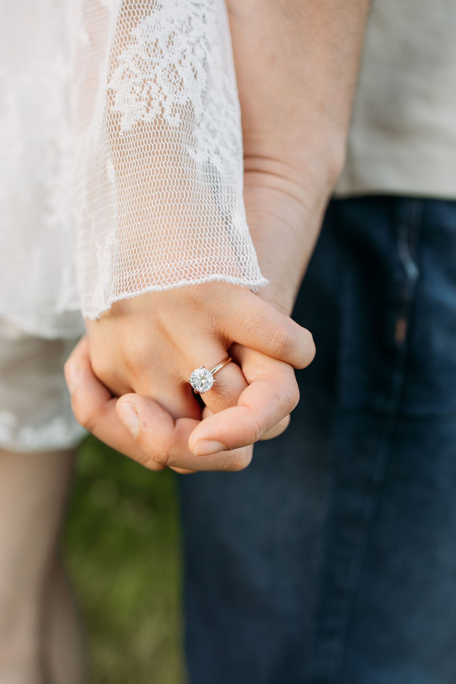 Close-up of a hand wearing an engagement ring with lace sleeve detail.