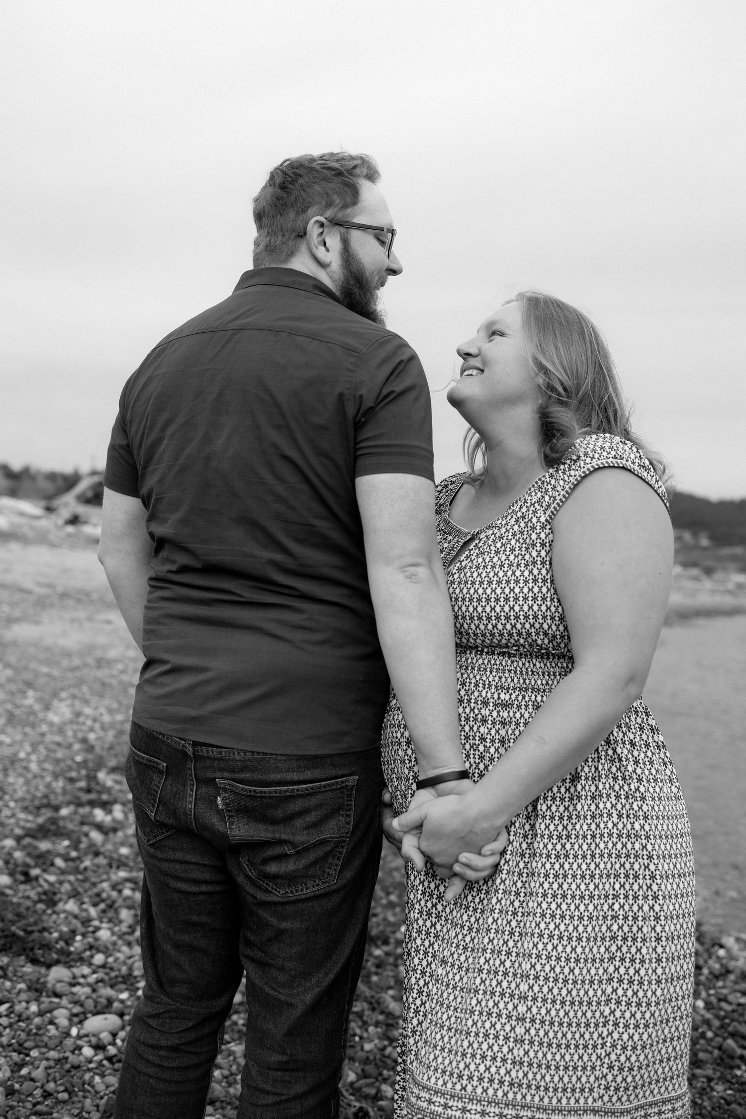 A happy couple shares a candid black and white moment together outdoors while holding hands.