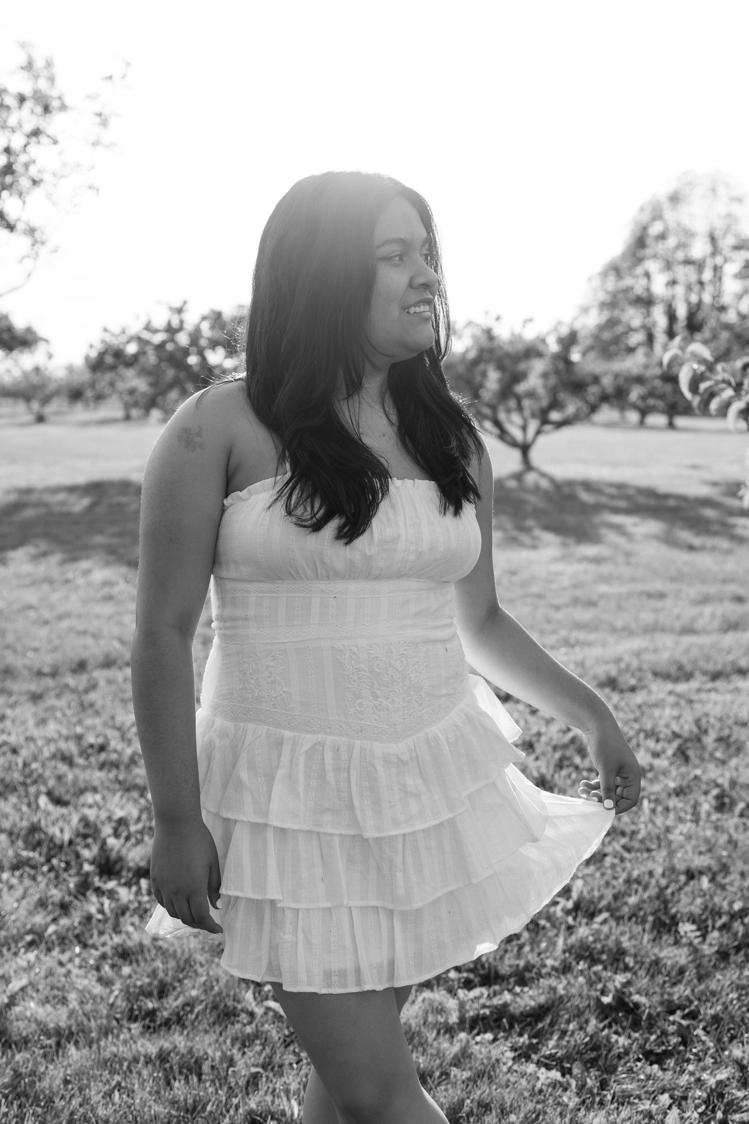 A joyful summer portrait showing someone in a white tiered sundress posing outdoors in a grassy field.