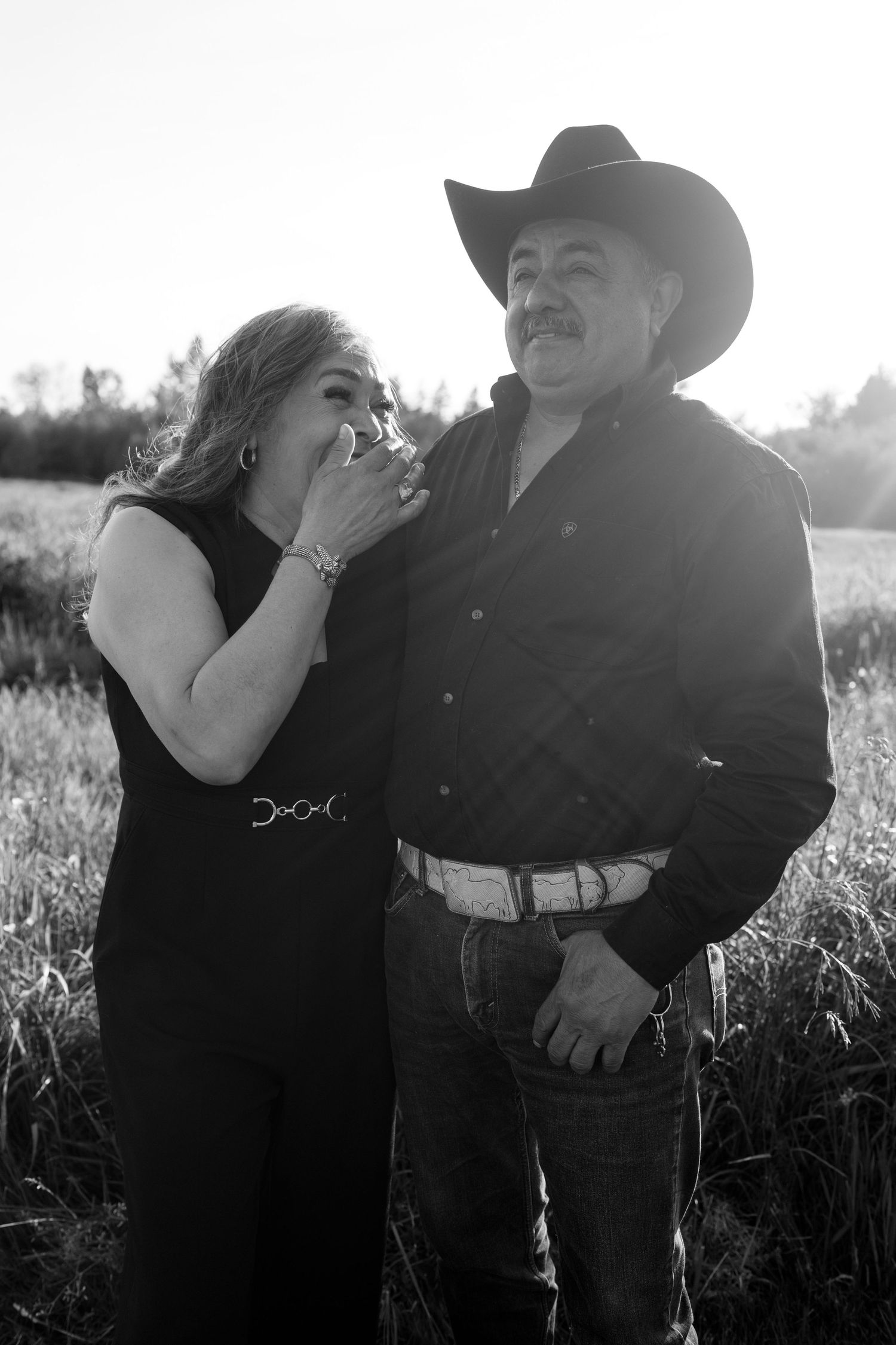 Romantic couple in western attire embraces in a sunlit field for an engagement photo session.