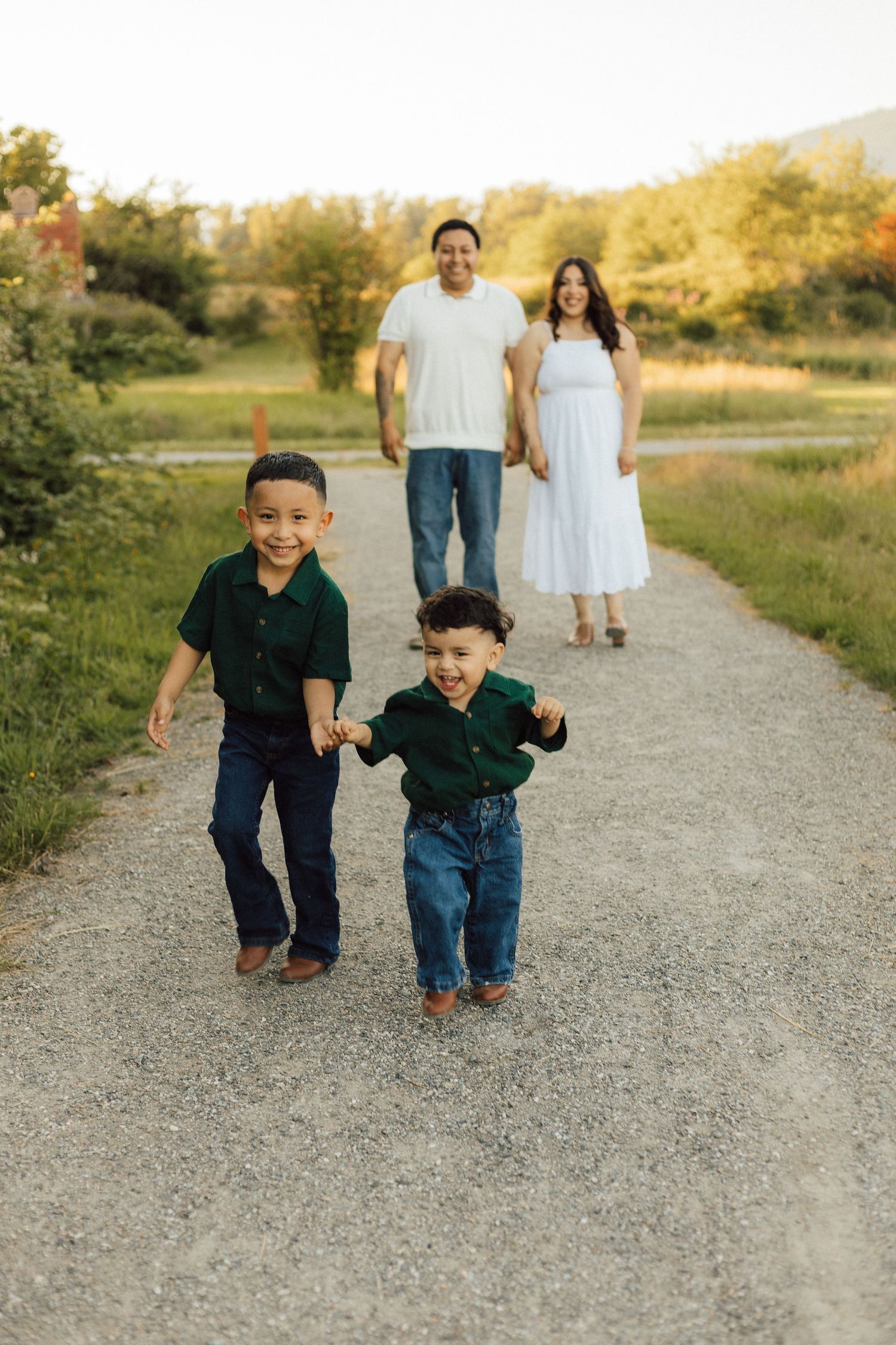 Two children run and play together on a gravel path in a sunny outdoor setting at sunset.