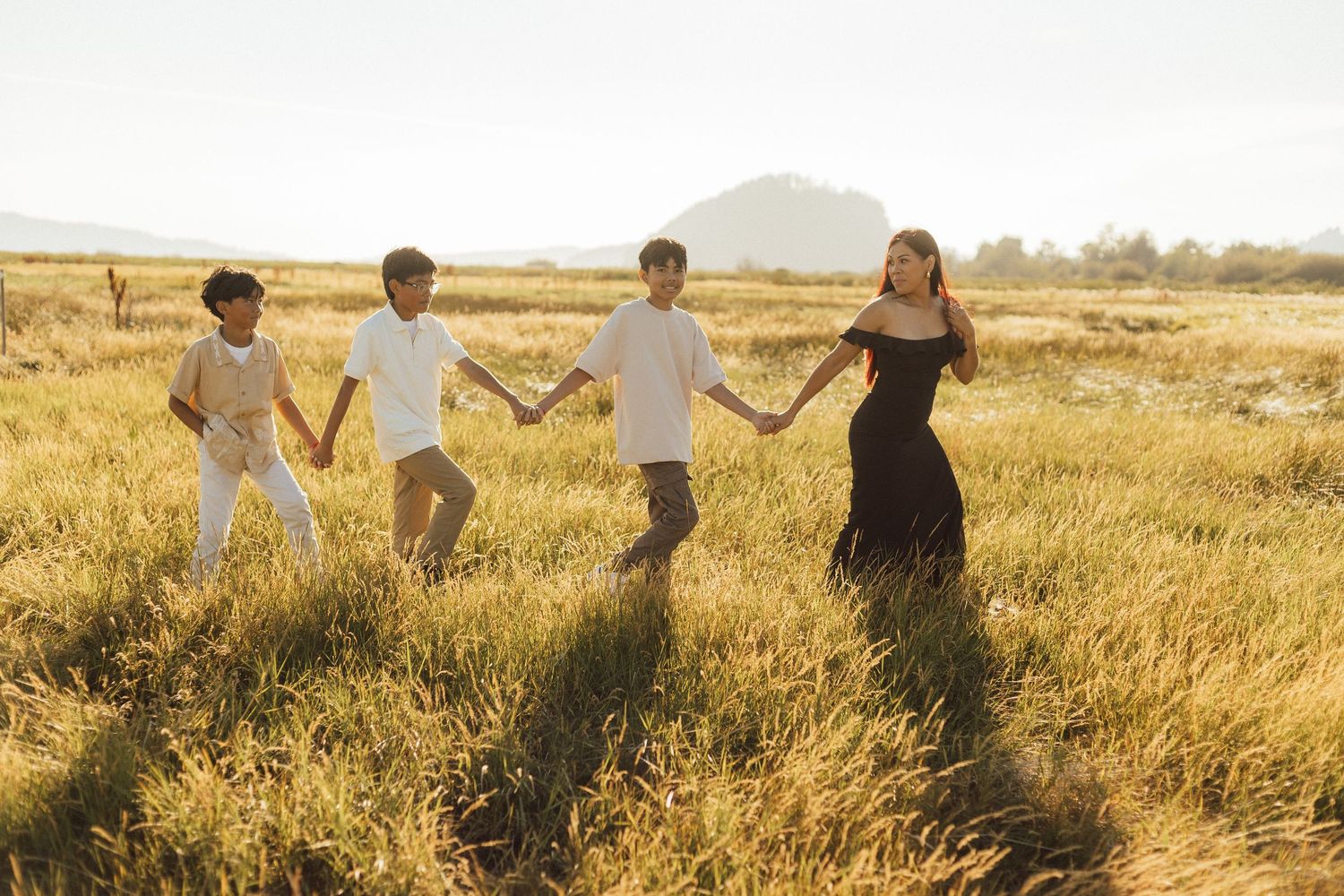 Group of people holding hands while walking through a golden field at sunset, creating silhouettes against the warm sky.
