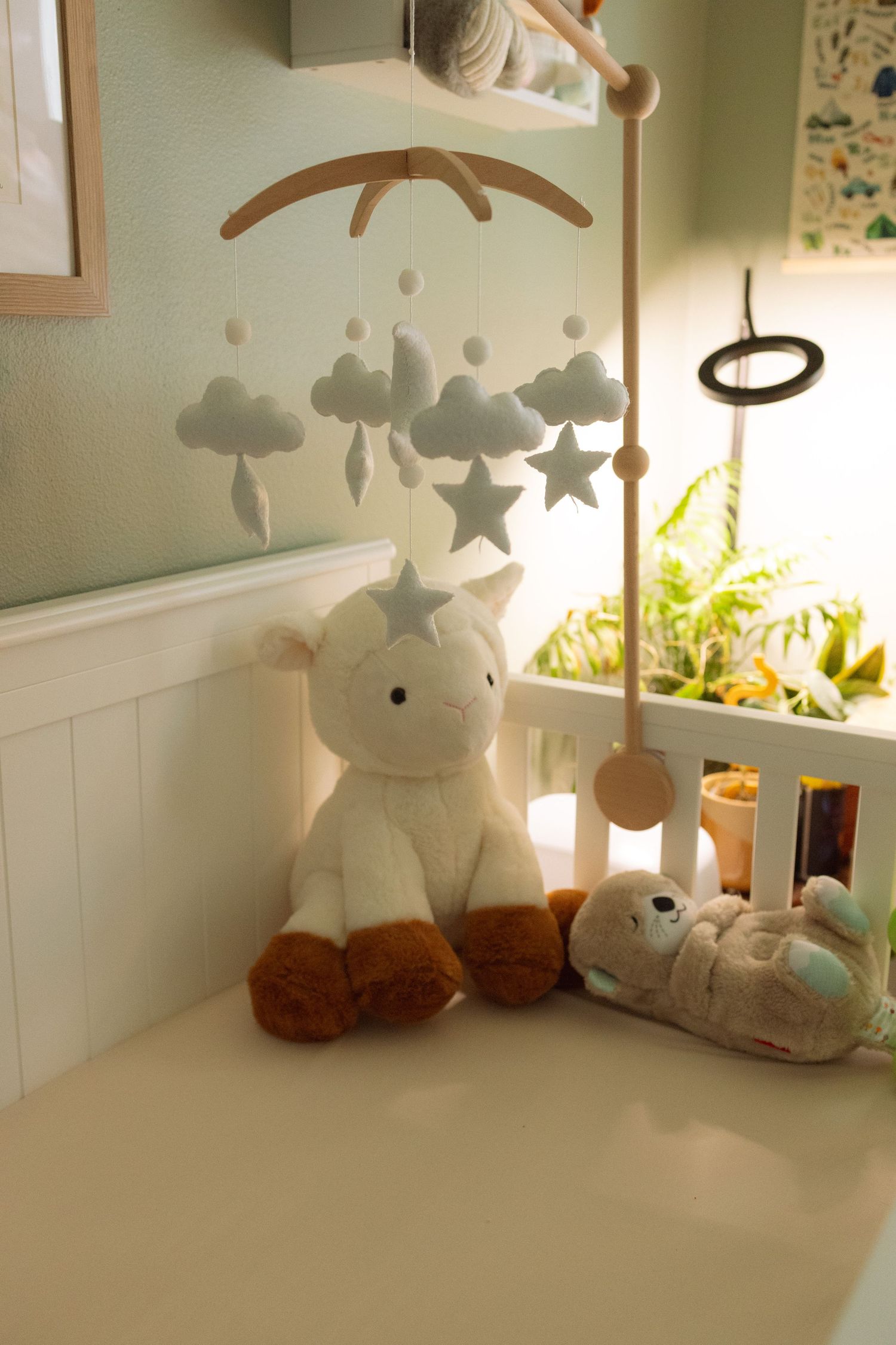 Baby nursery decor featuring white plush toys, mobile with clouds and stars, and soft natural lighting.