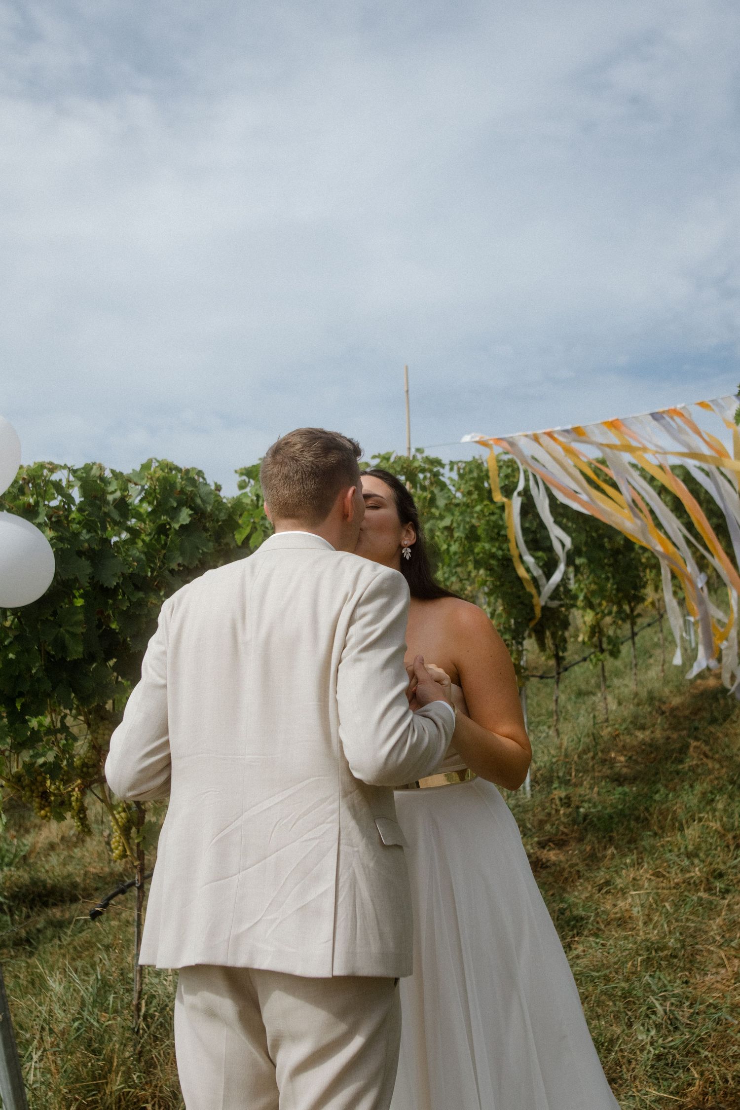 Couple embracing in a vineyard with decorative streamers and balloons in the background.