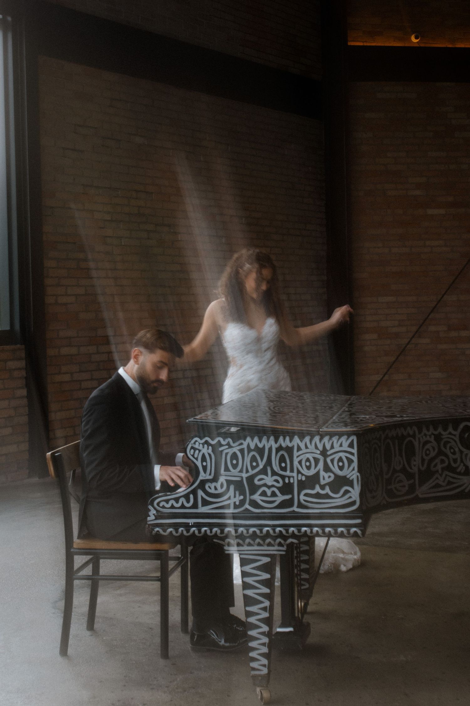Artistic motion blur photo of couple at grand piano in industrial brick venue.