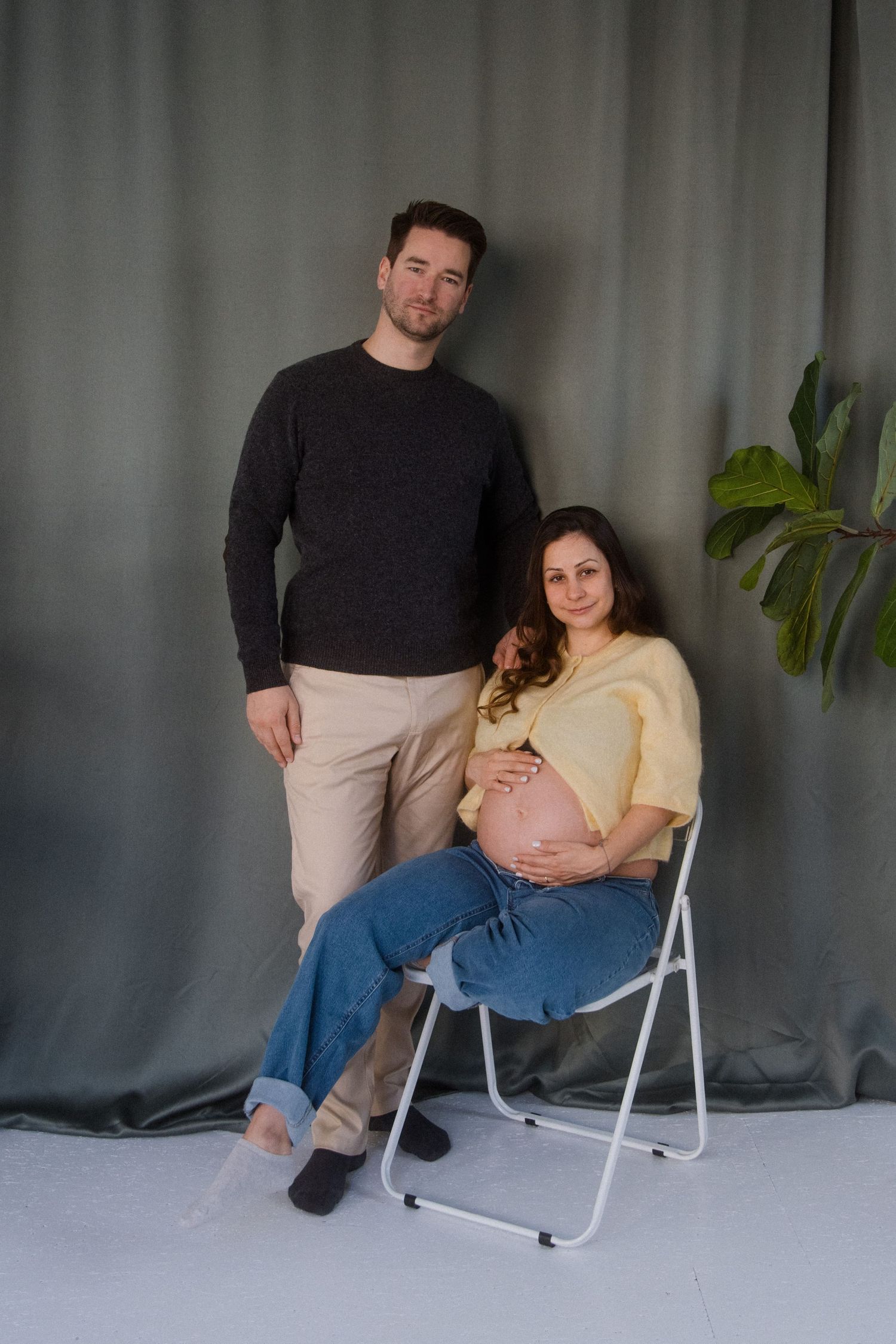 A couple sits together in a series of progressive poses on a white chair against a gray backdrop.