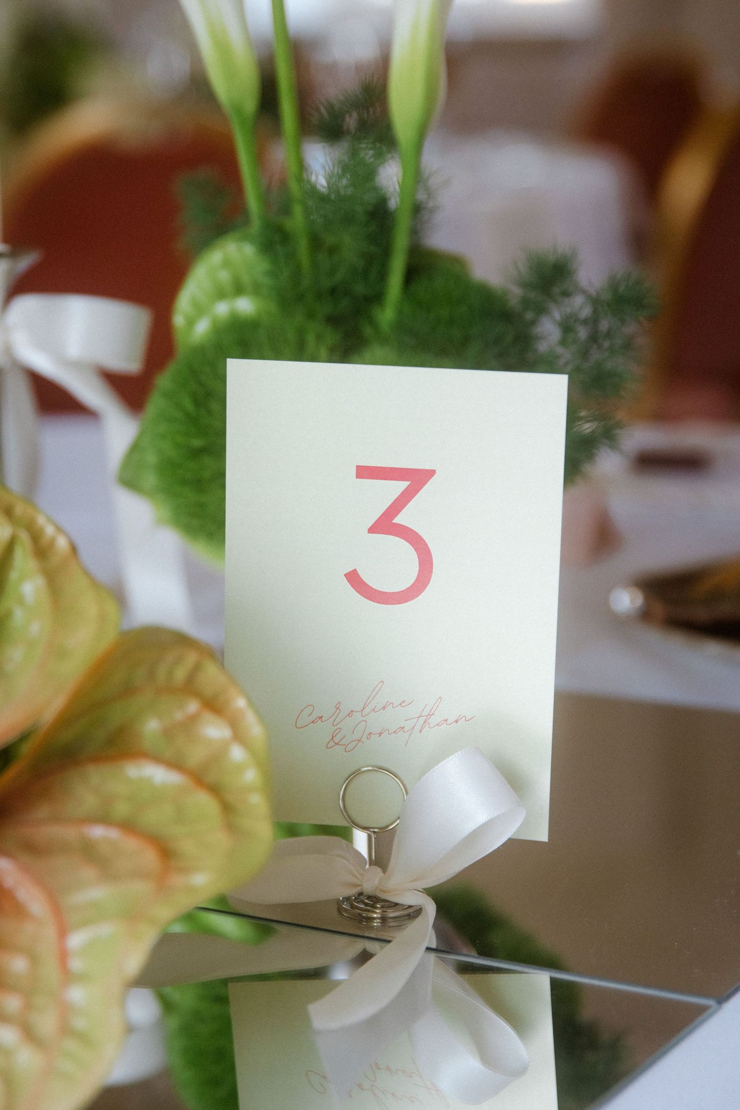 Table number cards and floral arrangements with green foliage at wedding reception.