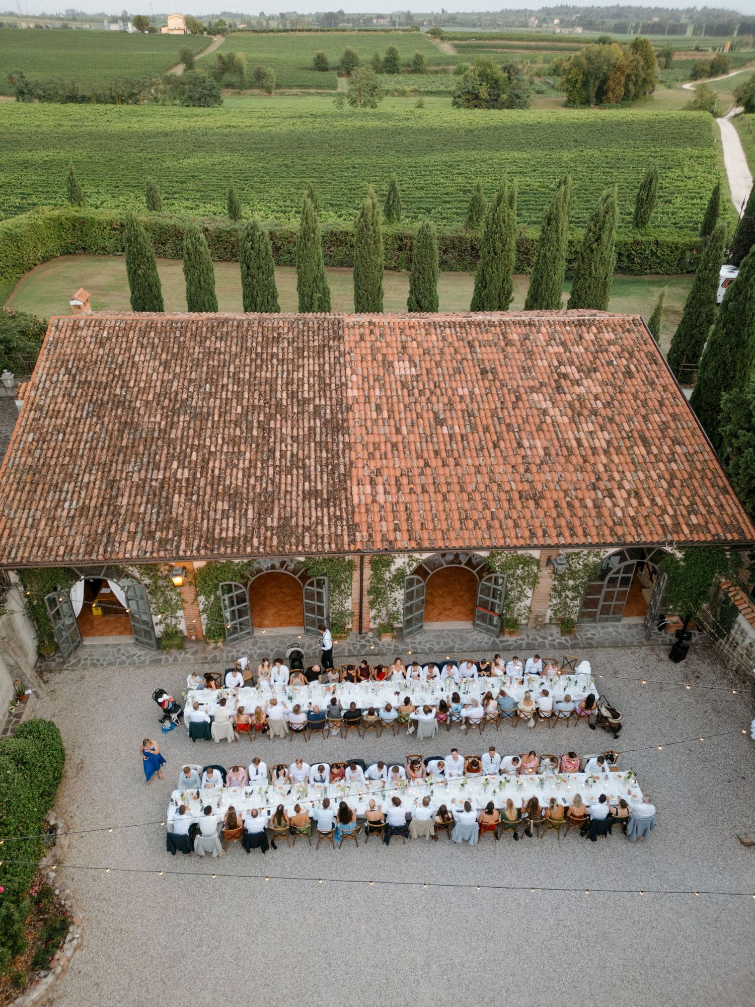 Aerial view of wedding reception setup against a rustic building surrounded by cypress trees.