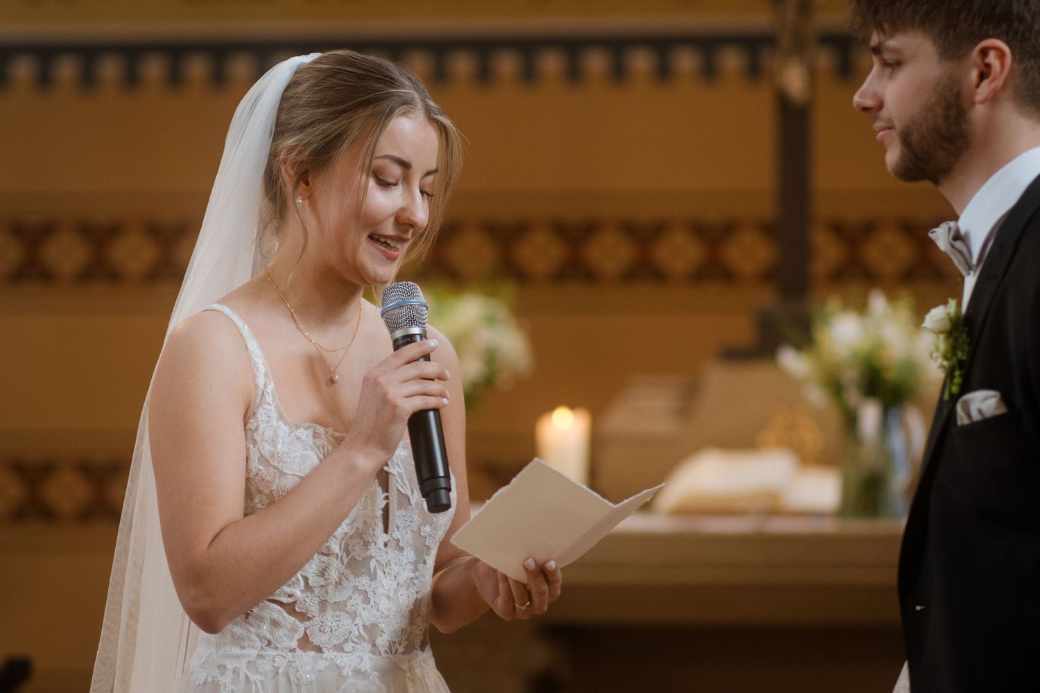 Bride reading heartfelt vows from paper during indoor wedding ceremony.