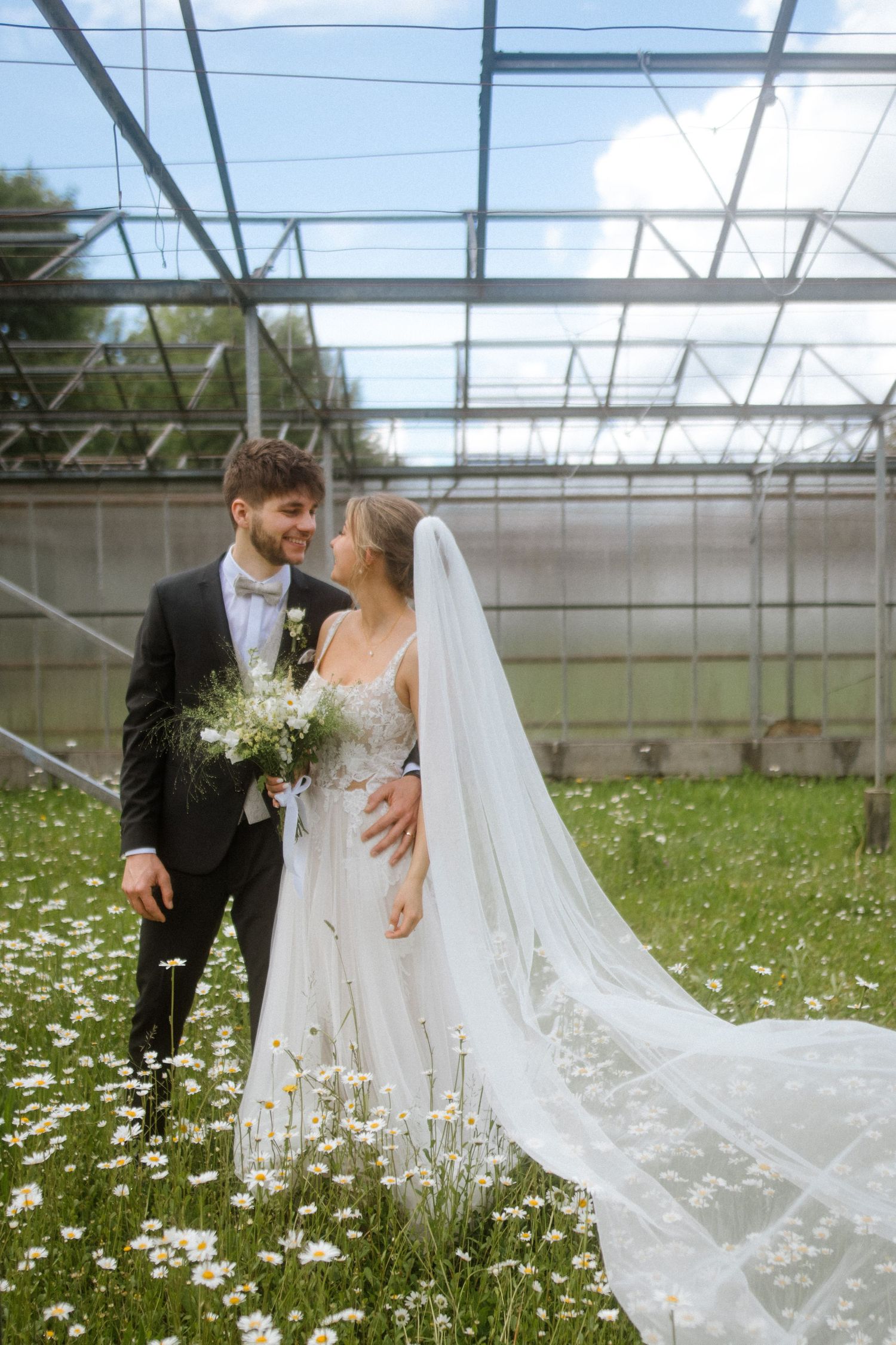 Newlyweds share a tender moment in greenhouse surrounded by wildflowers.