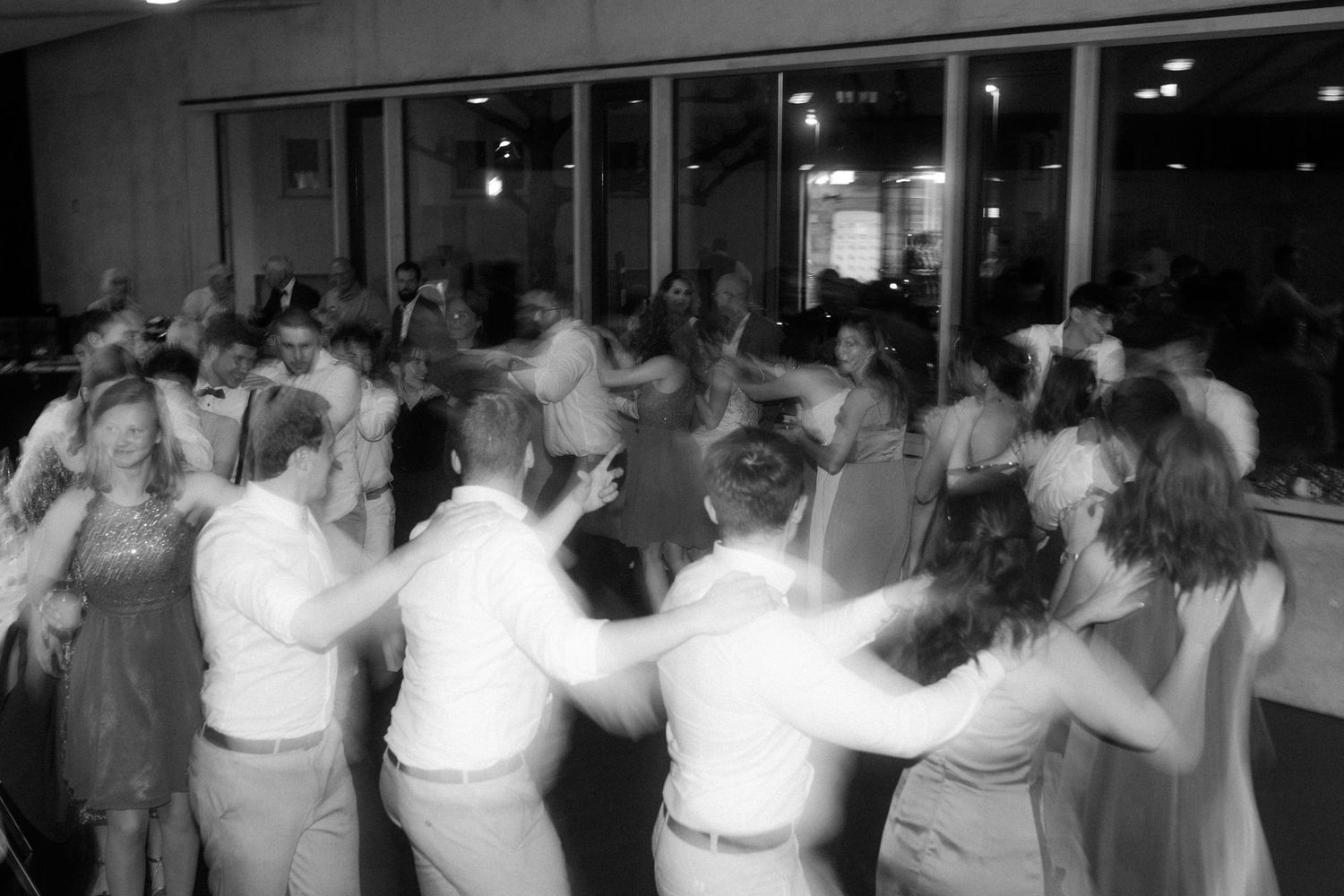 Black and white photo of wedding guests dancing in a circle during reception.
