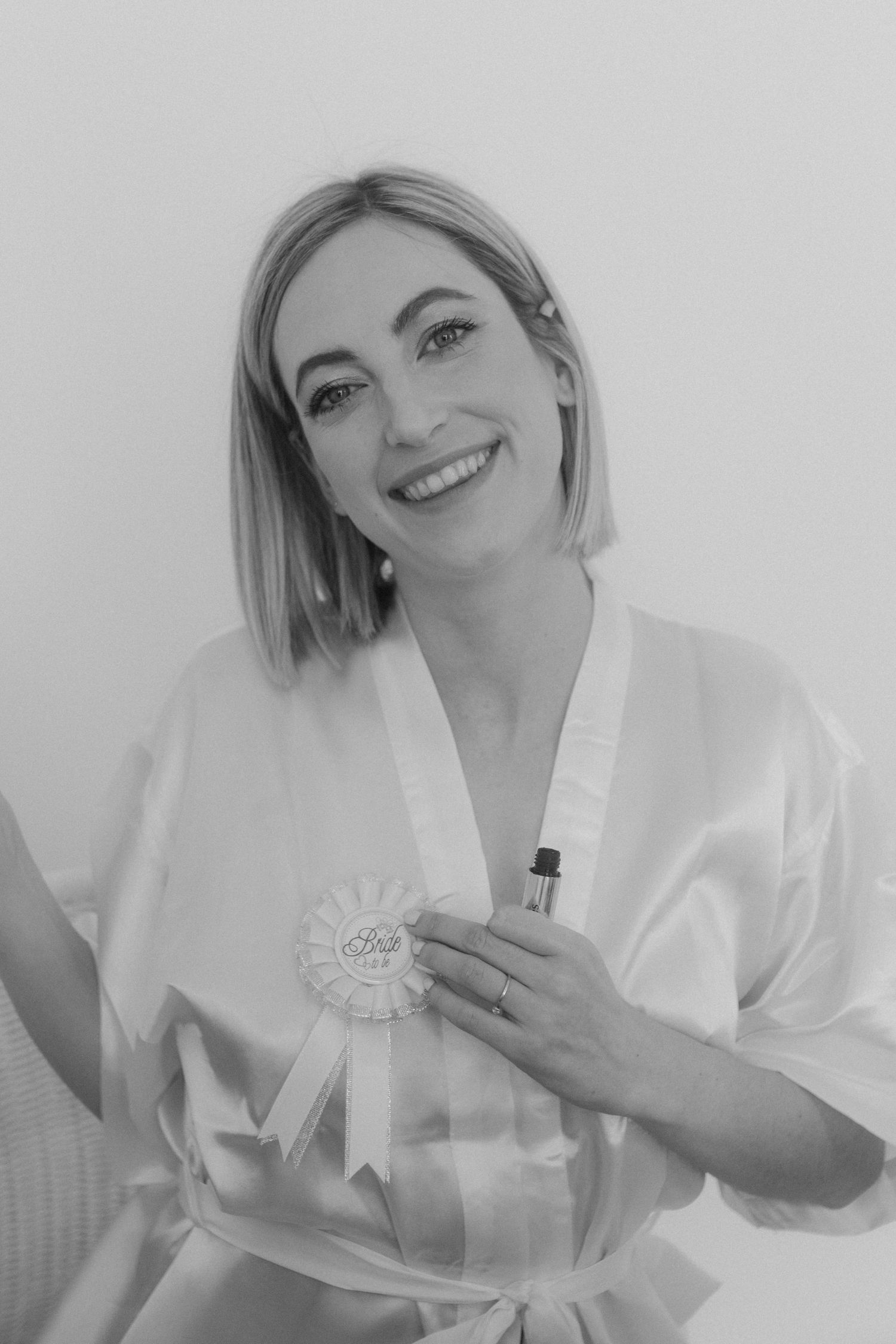 Person wearing white robe holds celebratory badge while getting ready.