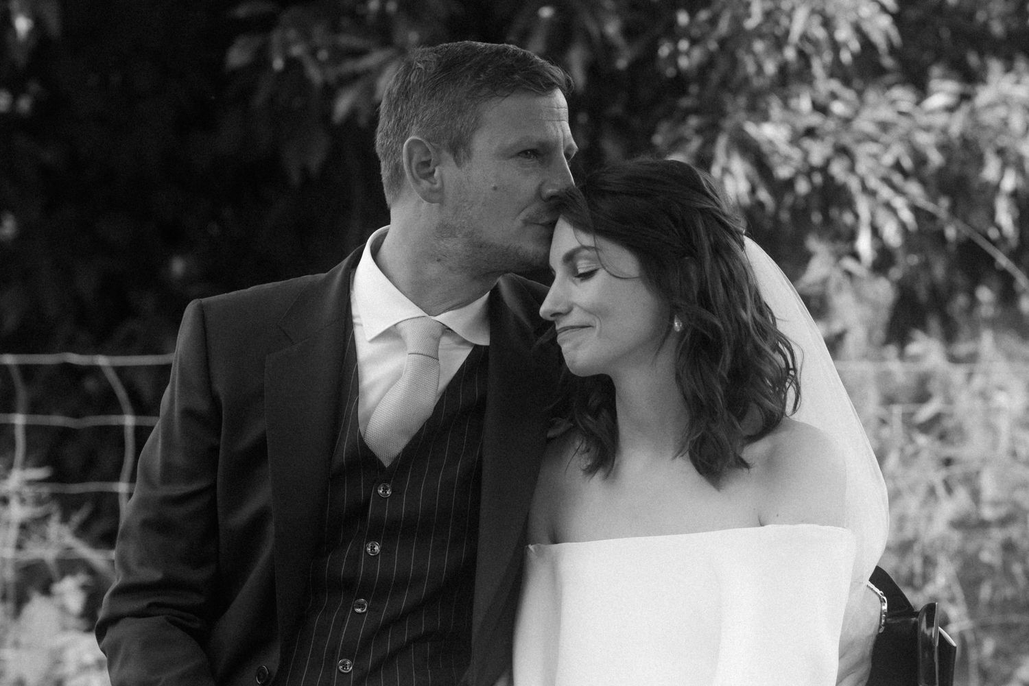 Intimate black and white portrait of newlyweds sharing romantic moment outdoors.