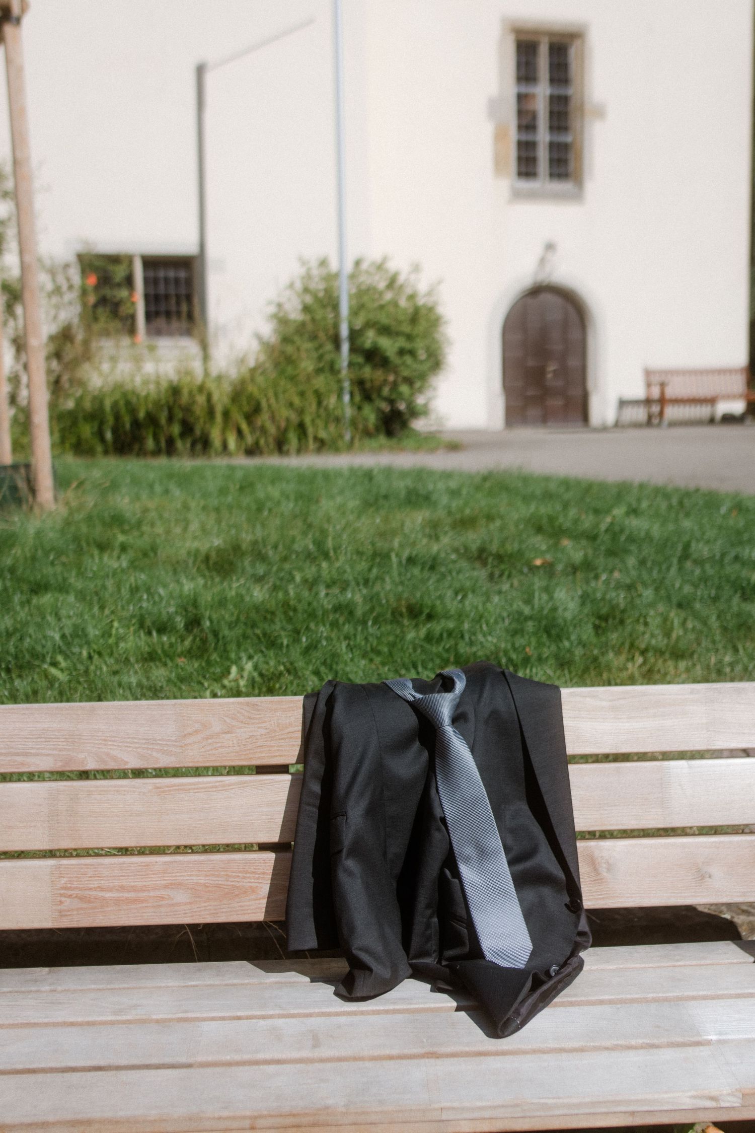 A formal suit jacket and tie laid out on a wooden bench with a white building in the background.