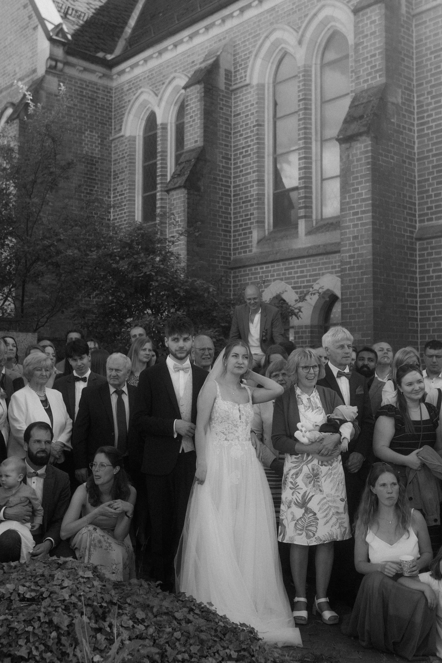 Wedding guests gather outside a traditional brick church building during an outdoor ceremony.
