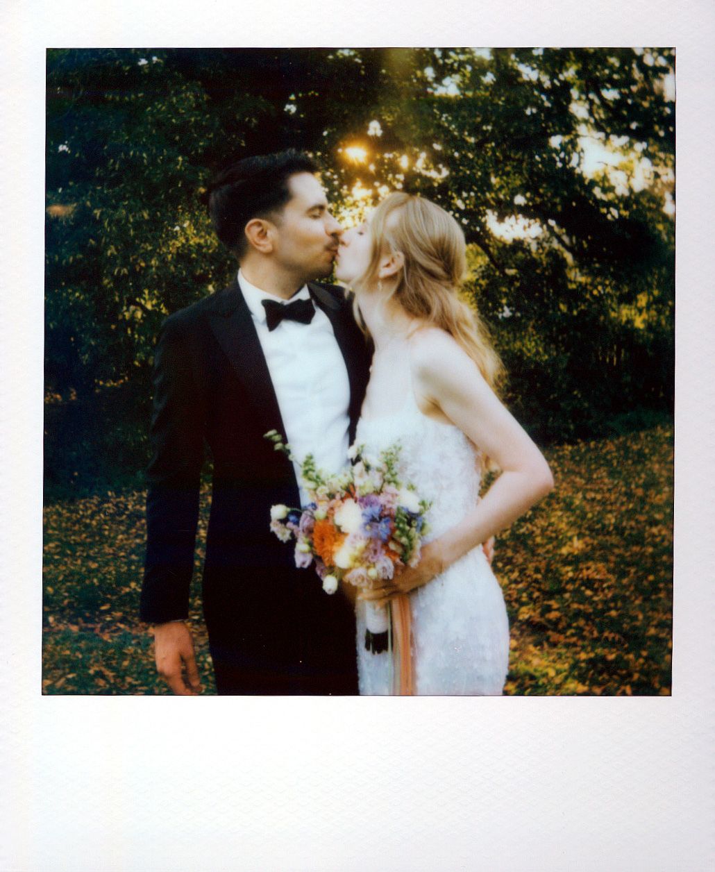 Romantic wedding couple embraces in an autumn garden setting with golden sunlight filtering through trees.