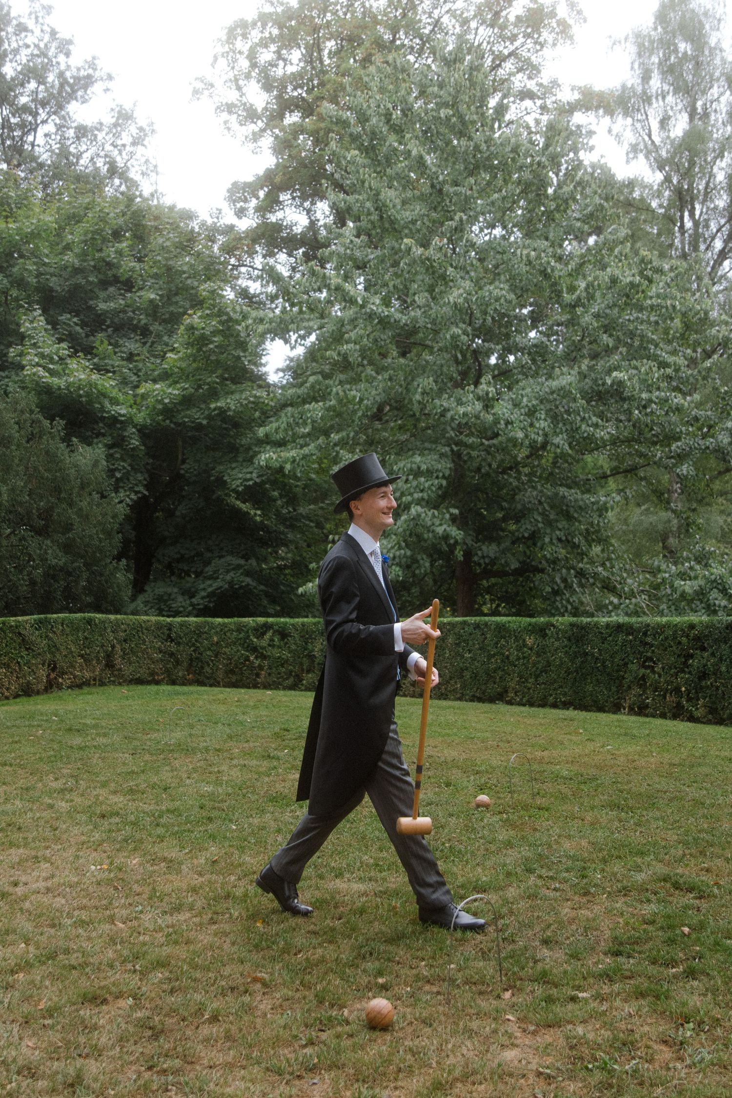 Person in formal attire taking a croquet shot on a grassy lawn.