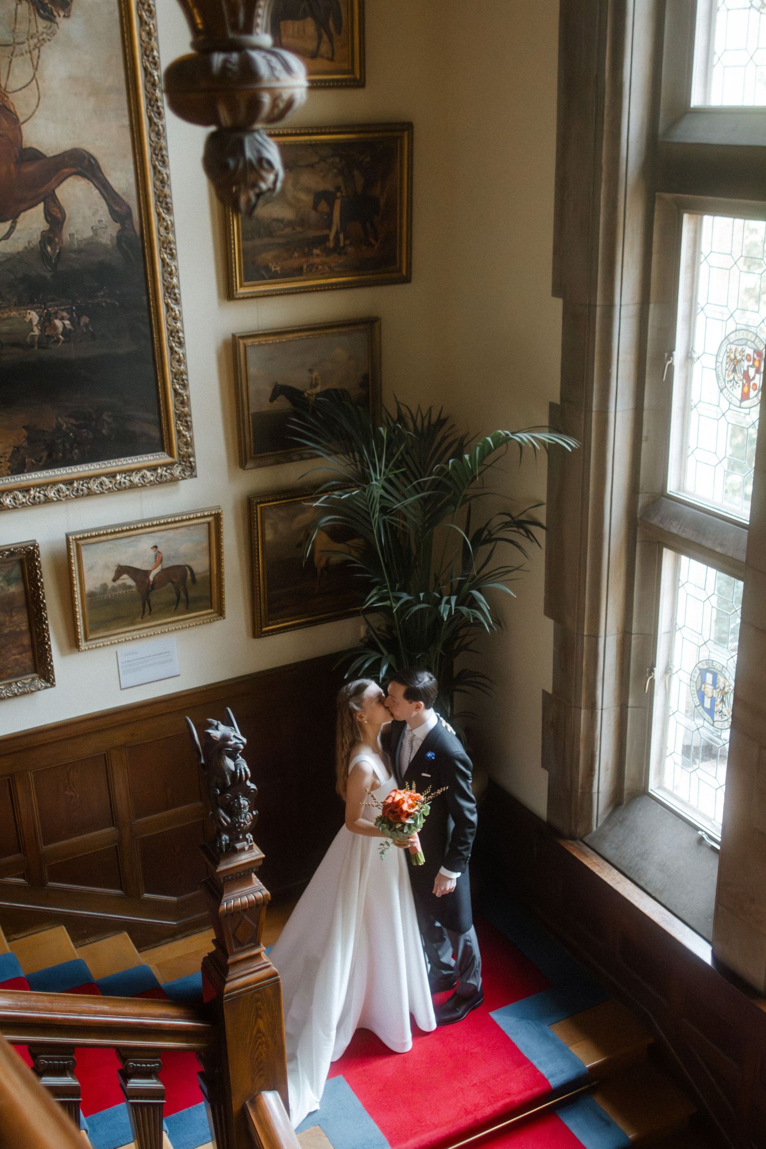 A romantic wedding moment beneath vintage equestrian artwork in a grand stairwell.