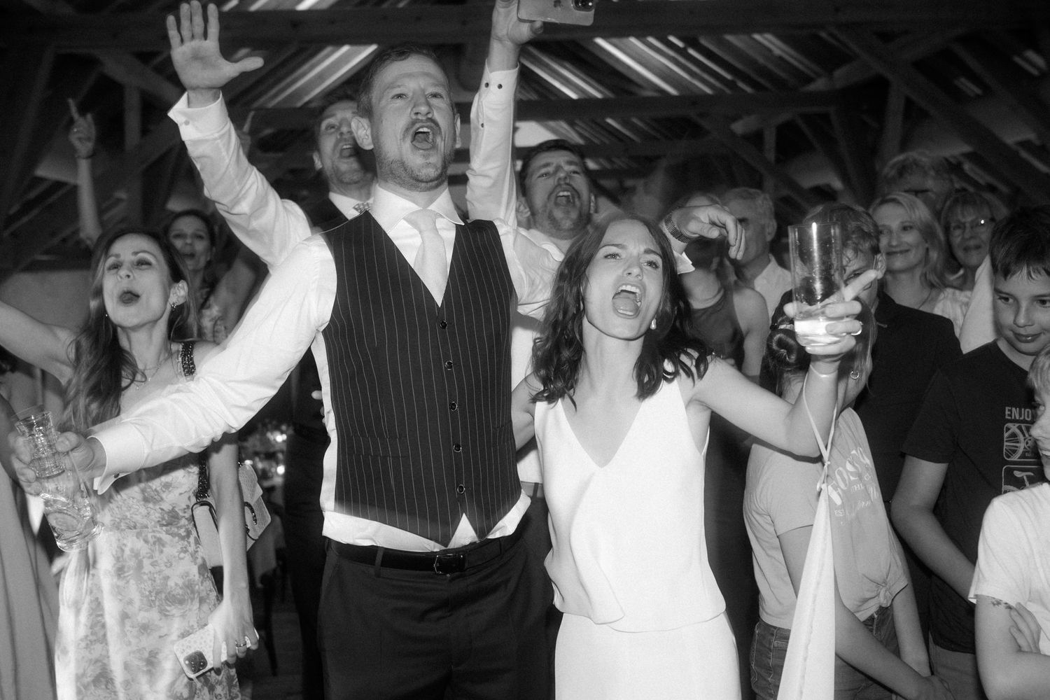 Couple celebrating with raised arms on dance floor in black and white photography.