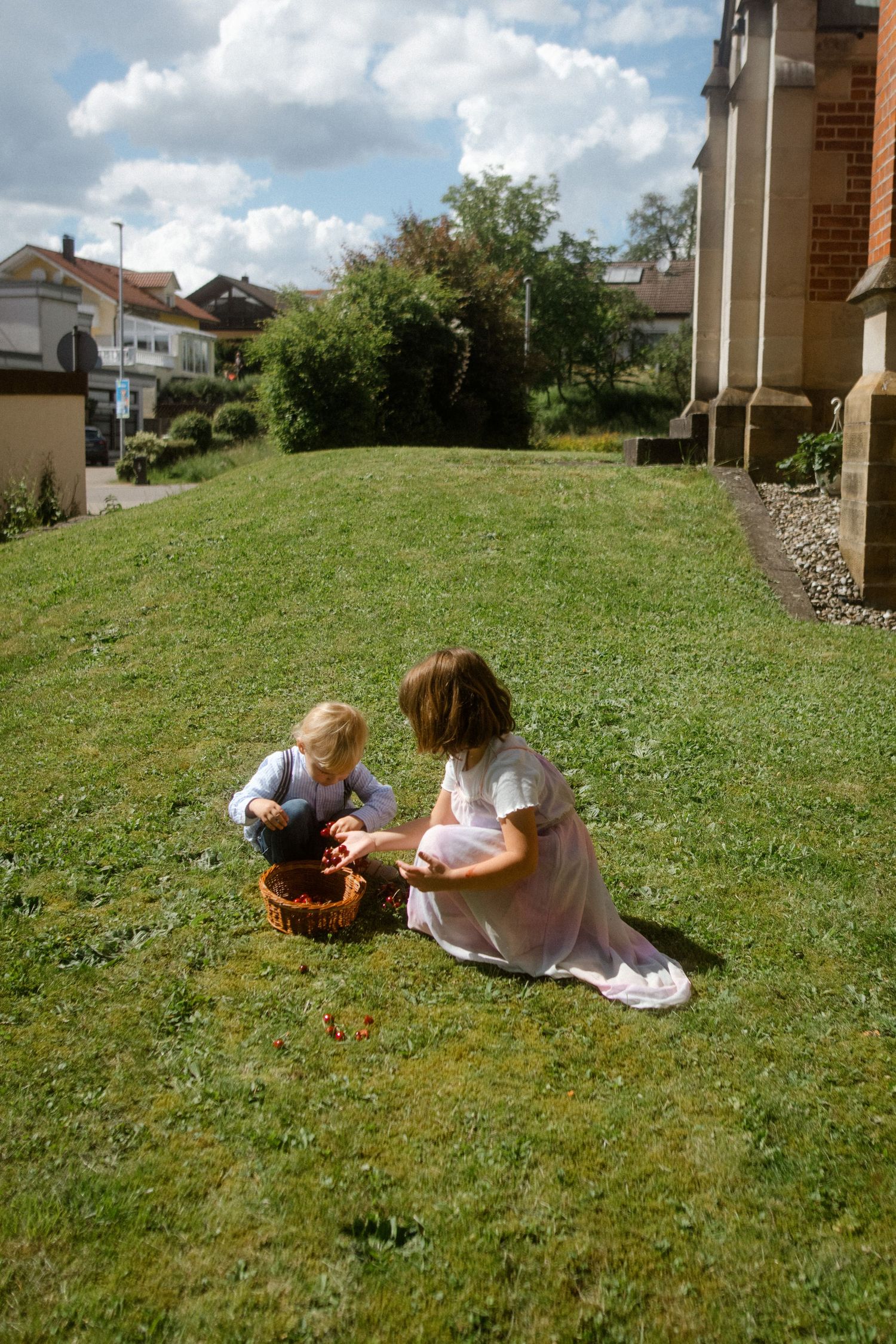 Two children sitting together on a grassy hill looking at something in a basket.