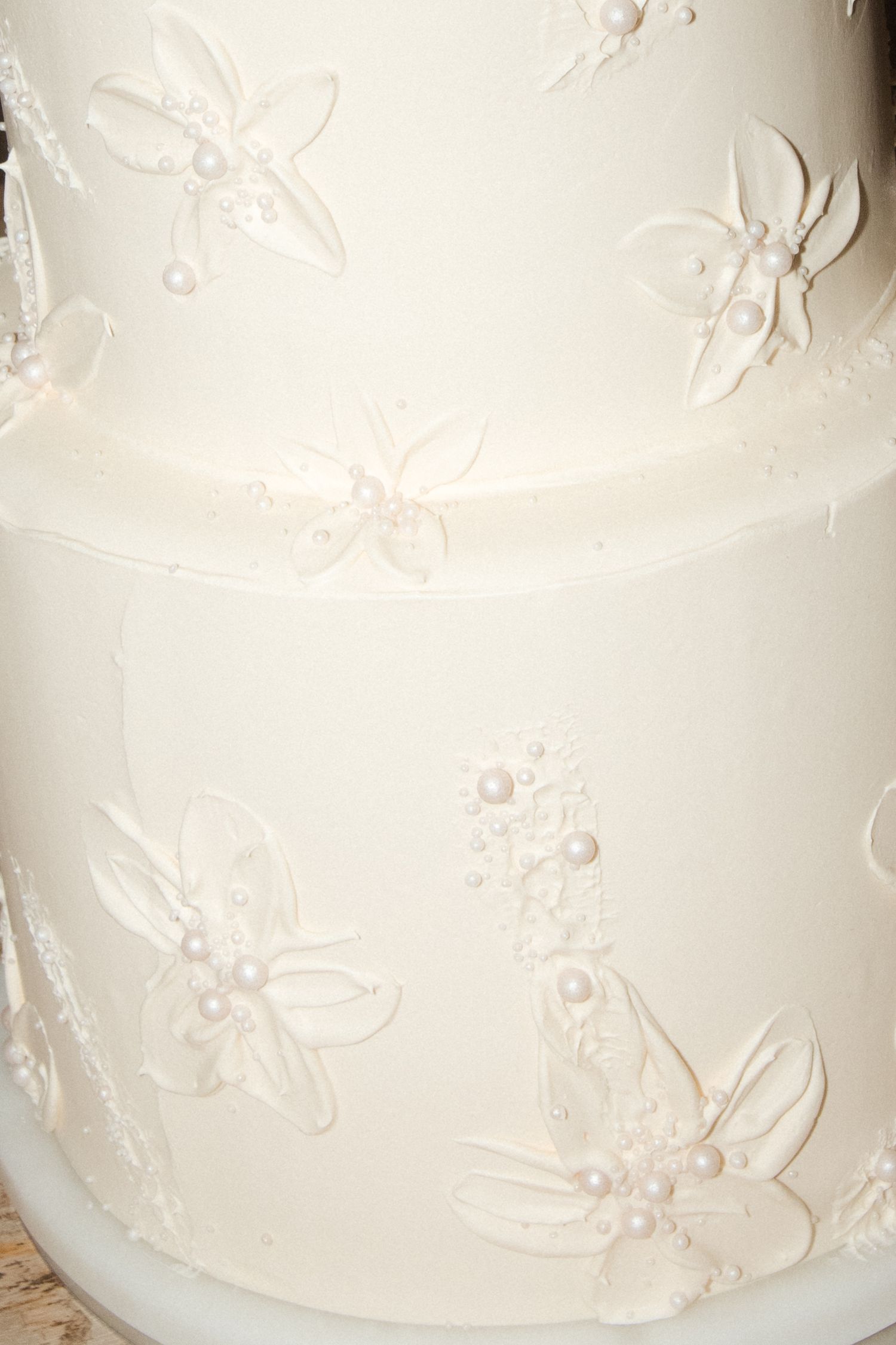 Close-up of white wedding cake decorated with raised floral pattern details.