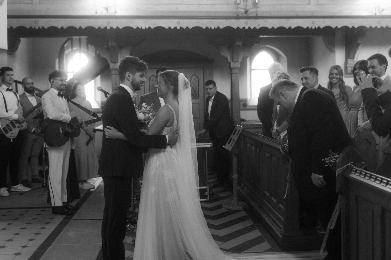 A black and white photograph captures an intimate wedding ceremony moment in a traditional church.