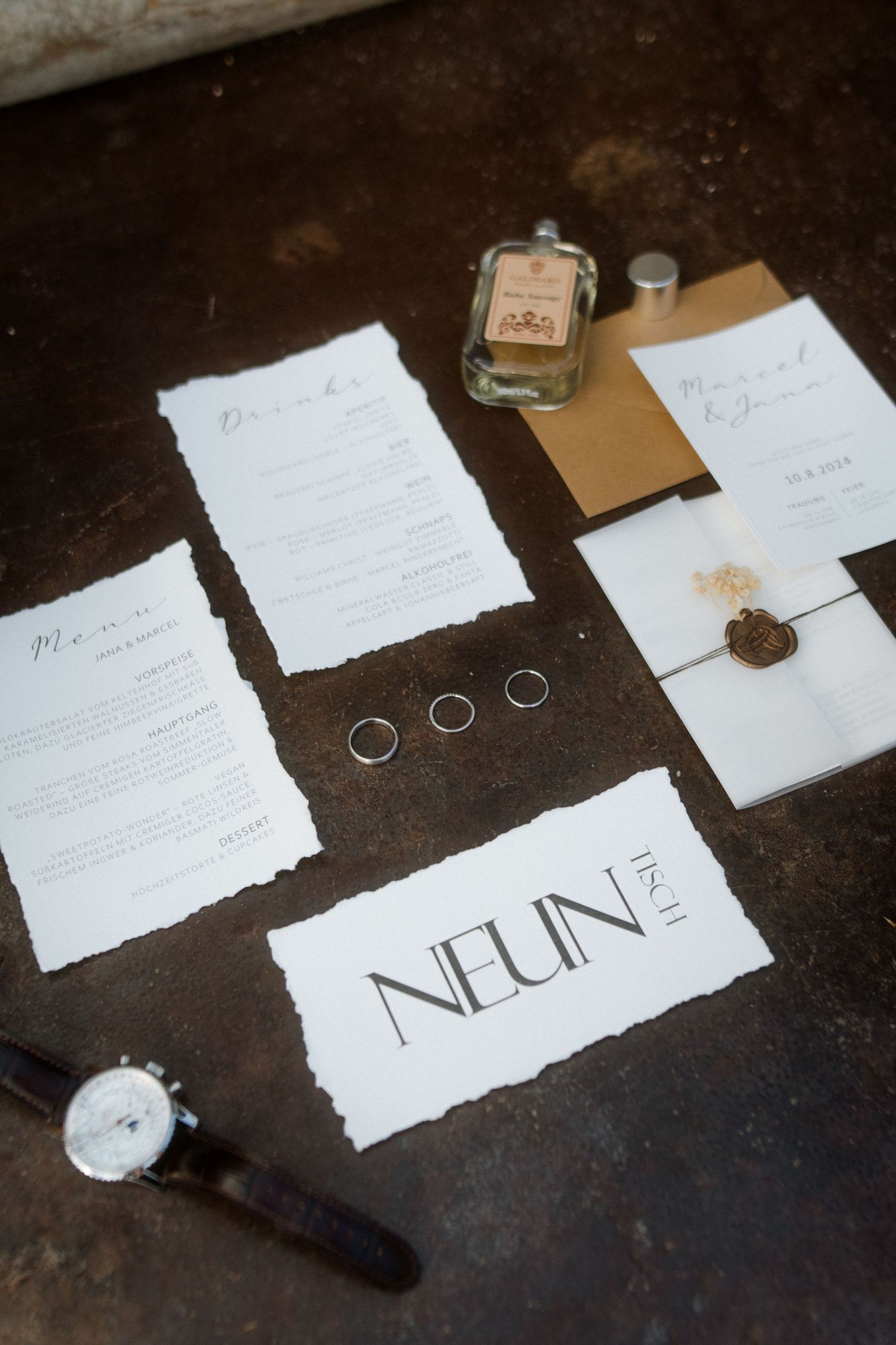 Wedding stationery flat lay with rings, wax seal, and Neun branding on dark surface.
