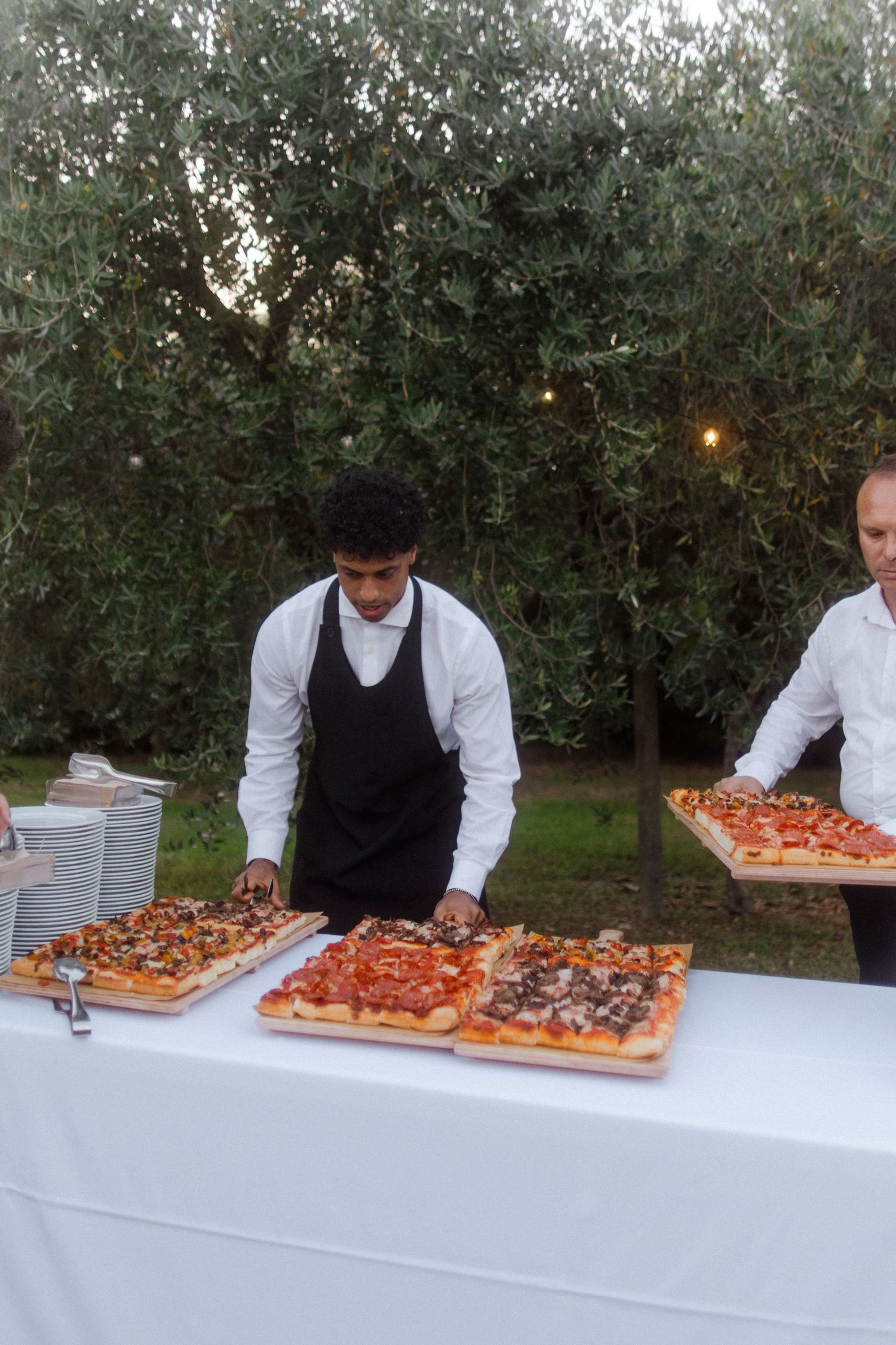 Long tables of appetizers and hors d'oeuvres being set up by servers at an outdoor event.