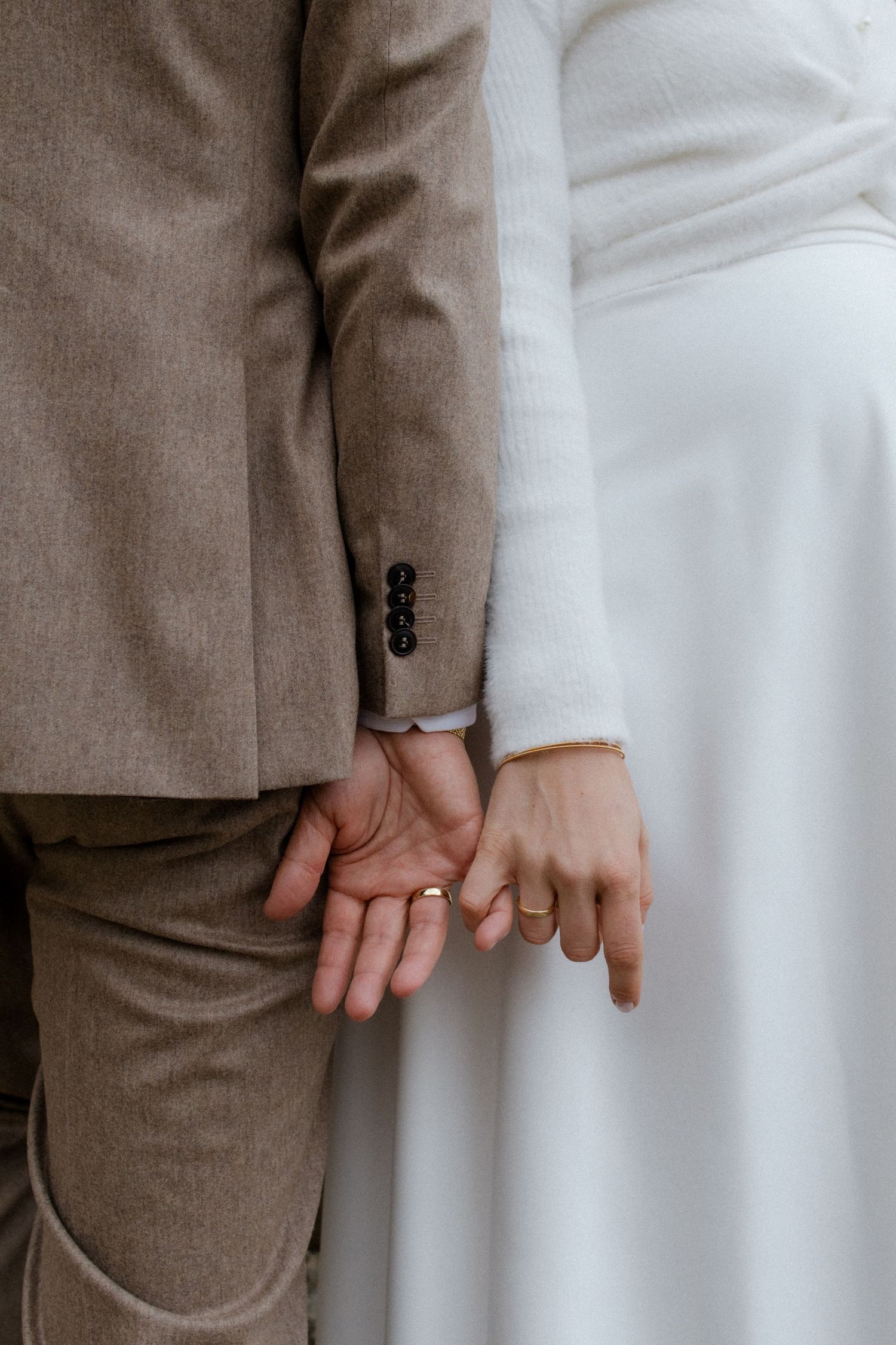 Close-up of couple holding hands showing wedding rings and formal attire.