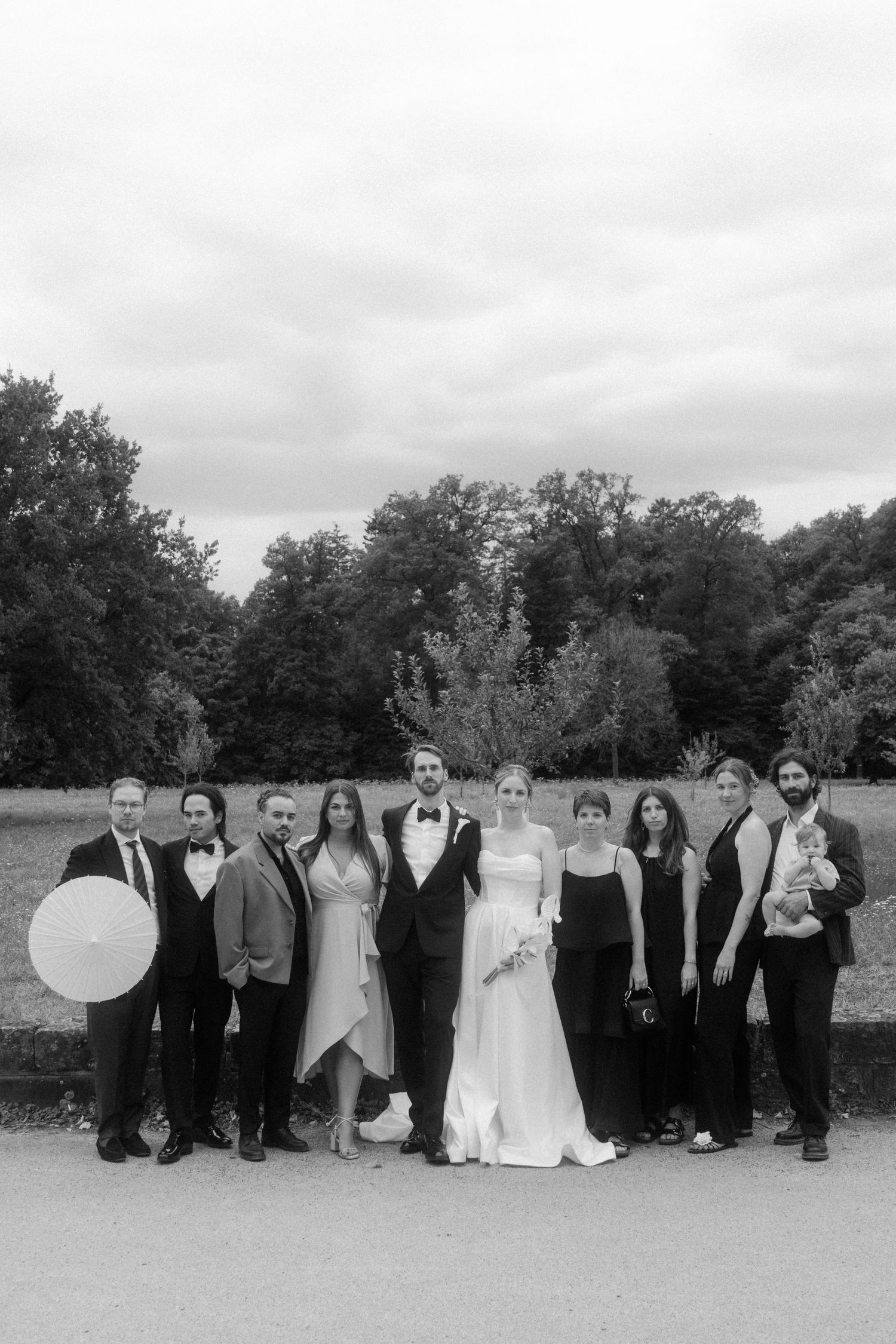 Wedding party members line up in formal attire against a natural outdoor backdrop.