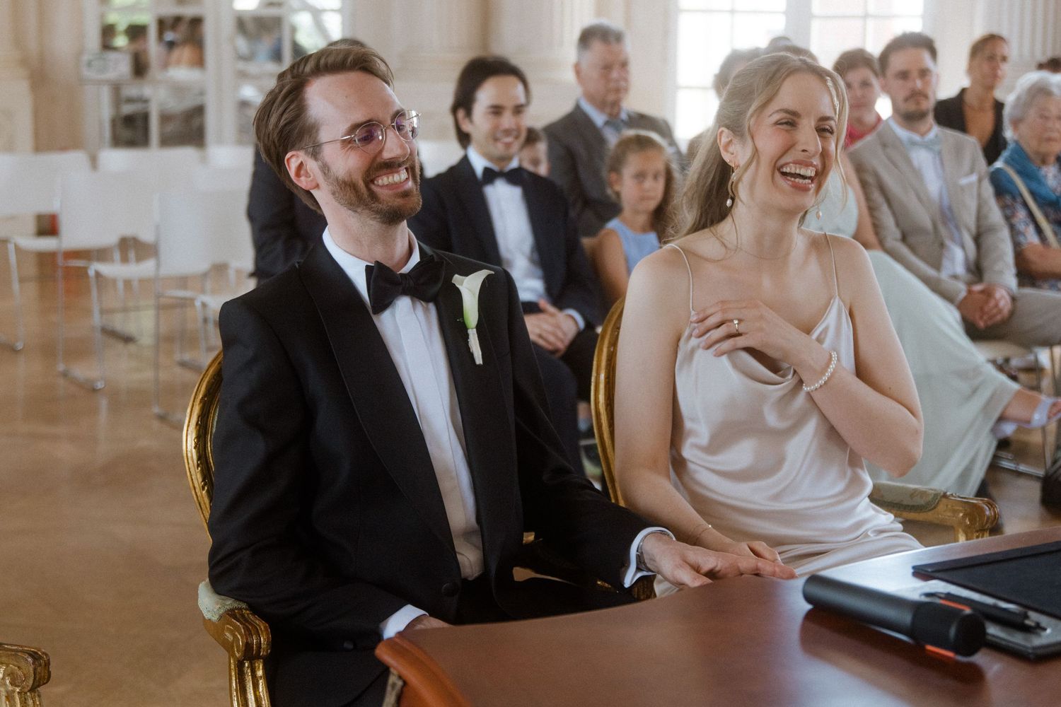 Wedding guests share joyful moments during the ceremony in a bright hall.