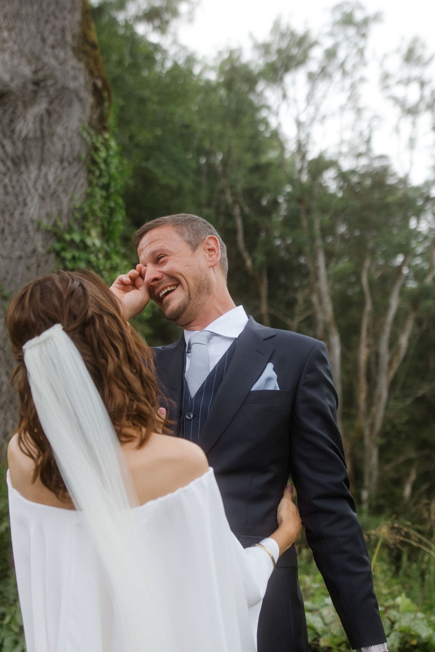 A couple shares candid laughing moments during their wedding photoshoot in a wooded setting.