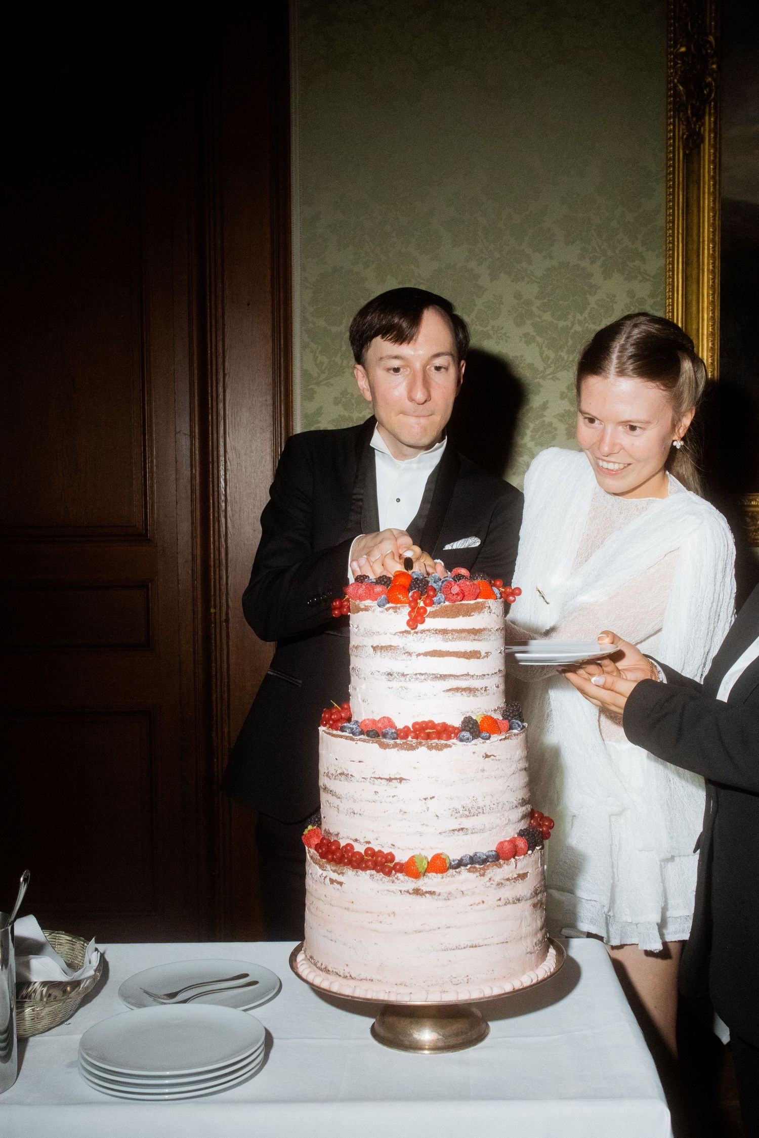 Couple cutting into their elegant three-tiered wedding cake decorated with fresh strawberries.