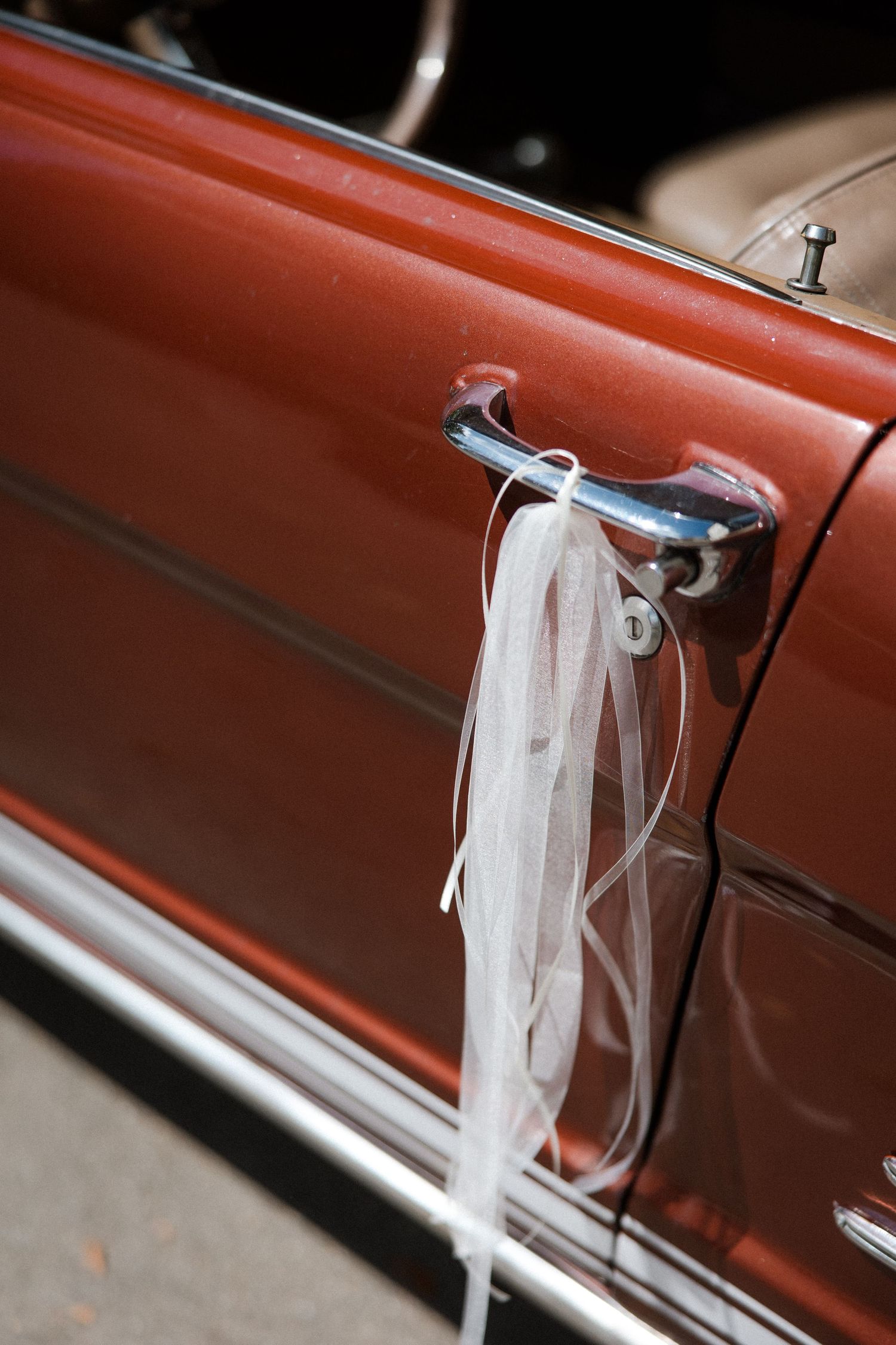 White wedding veil attached to vintage car door handle against copper-colored paintwork.