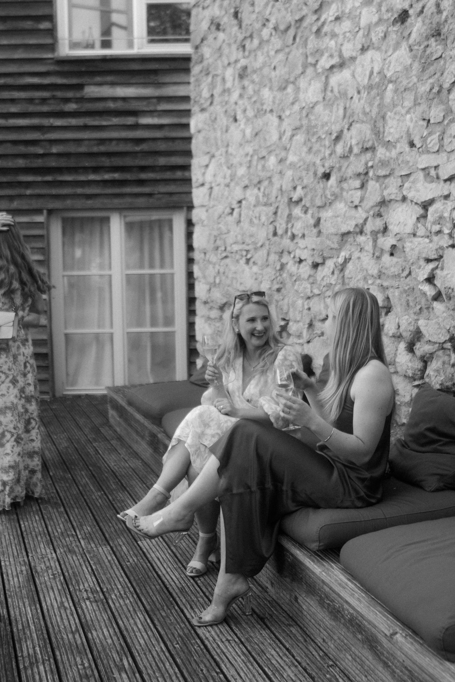 Two friends enjoying a relaxing conversation on a wooden deck with stone wall backdrop.