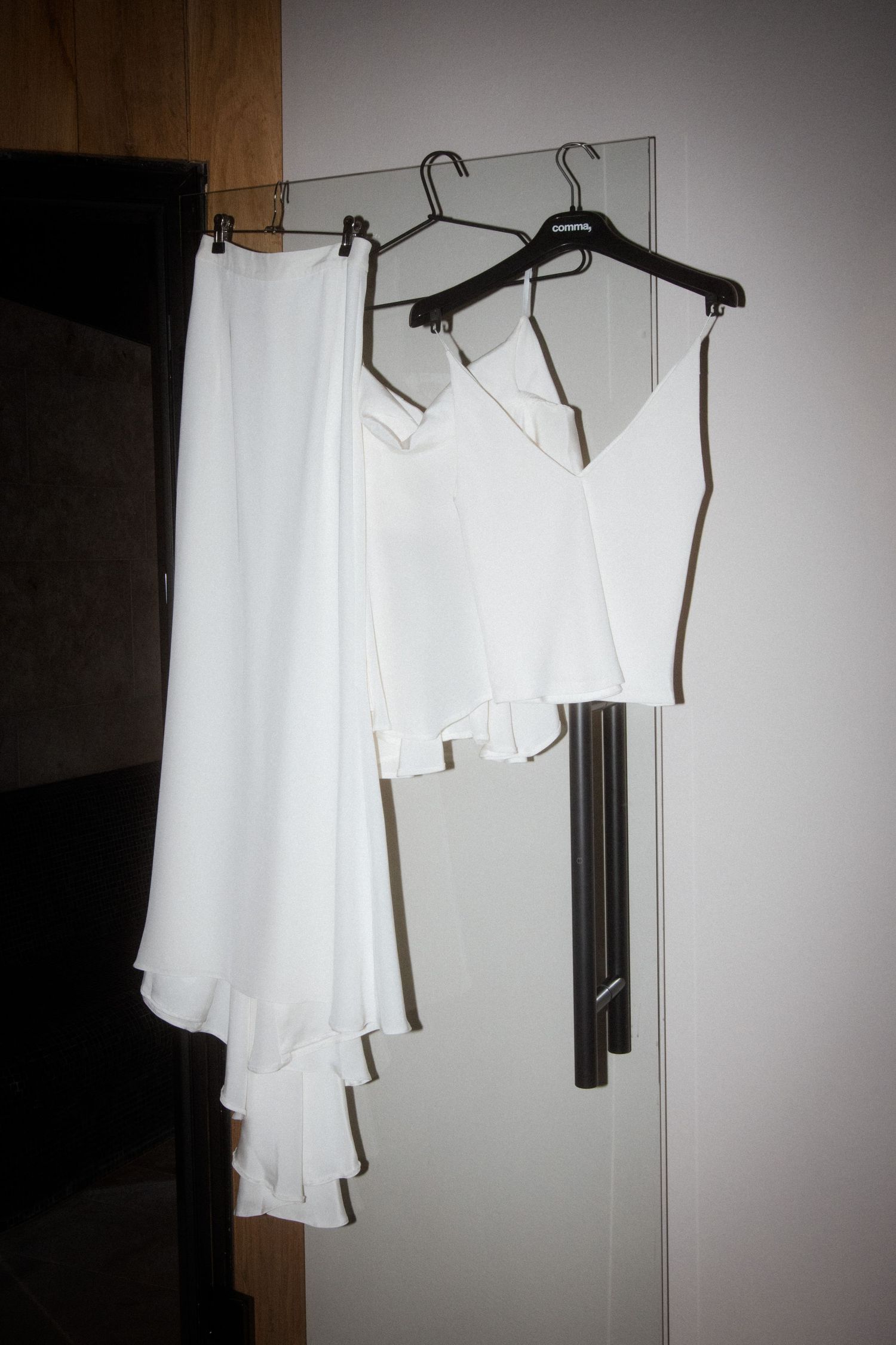 White formal attire hanging on black hangers against a wall.