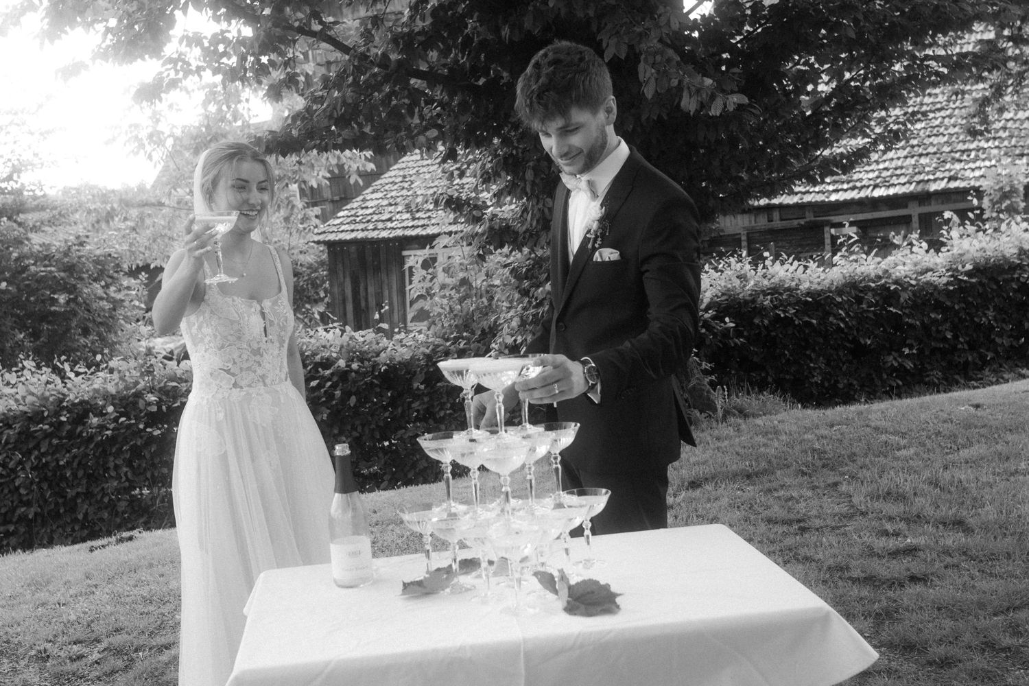 Black and white photo of wedding celebration with champagne tower outdoors.