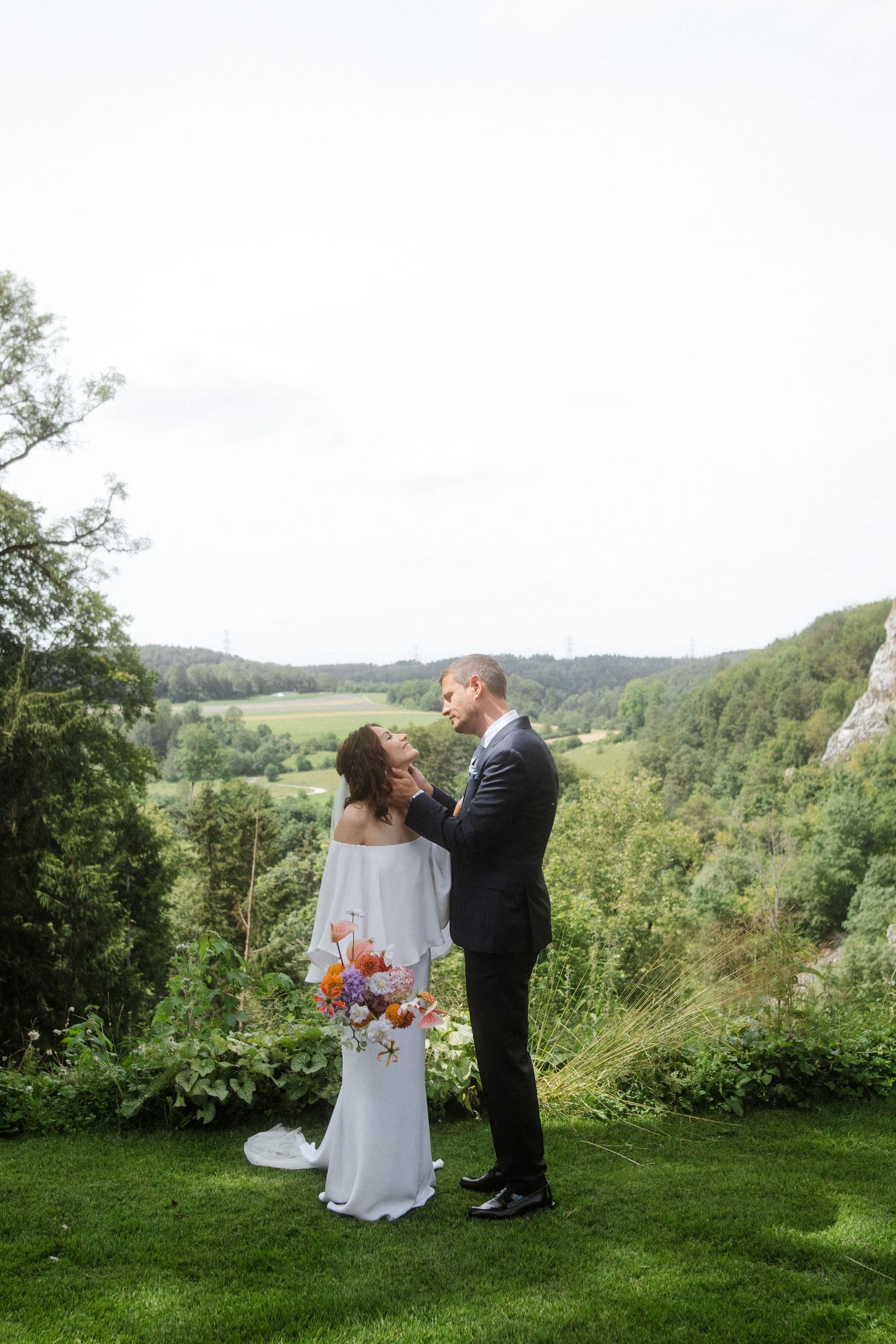 A romantic wedding moment captured on a scenic cliff overlook with rolling hills in the background.