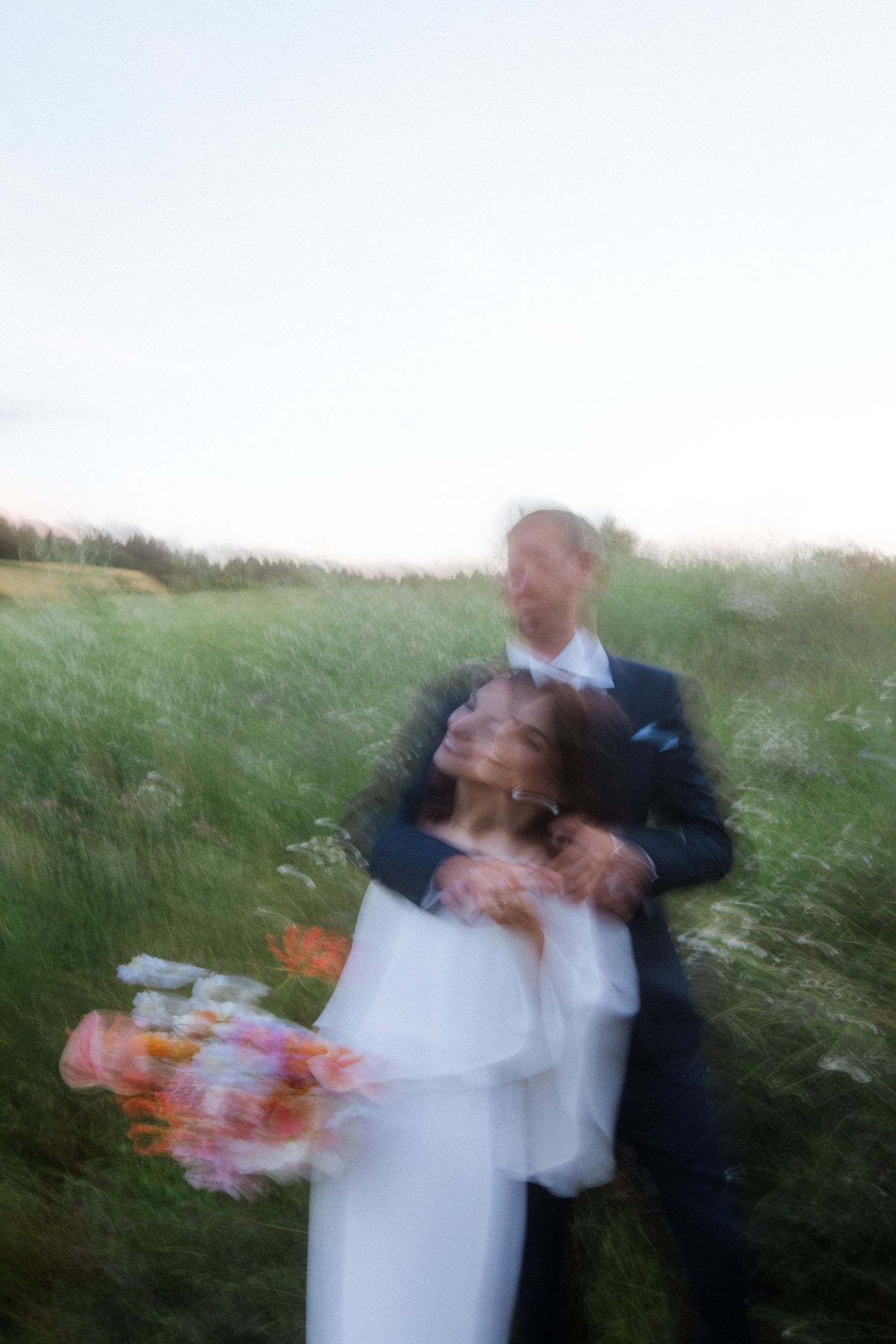 An artistic blurred photo of newlyweds dancing in a grassy field.