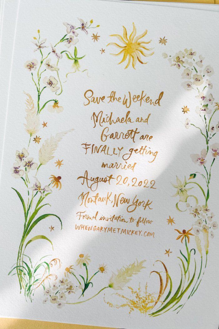 Elegant save the date invitation with watercolor floral border and gold calligraphy text.