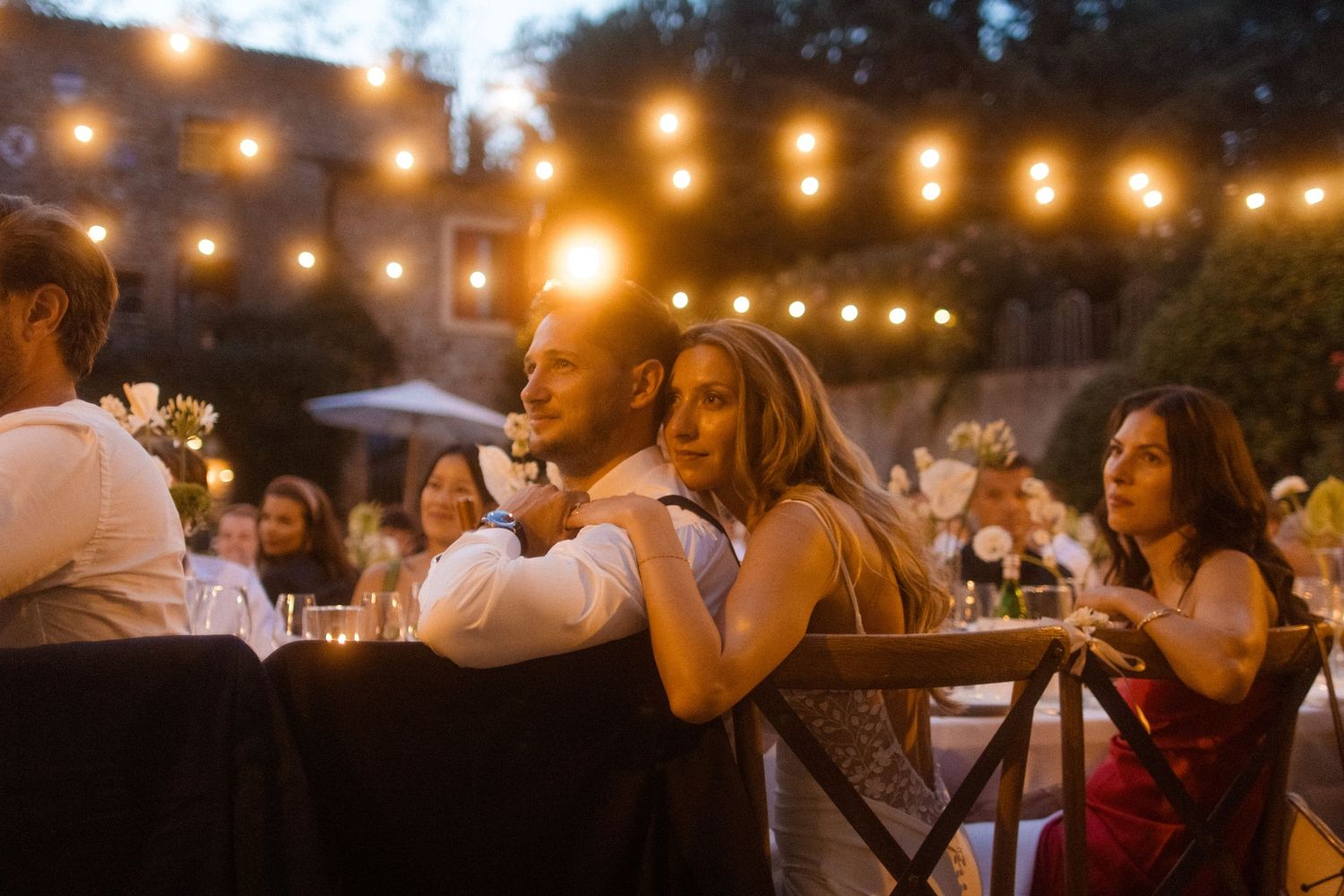Wedding reception guests enjoying dinner under warm string lights at dusk.