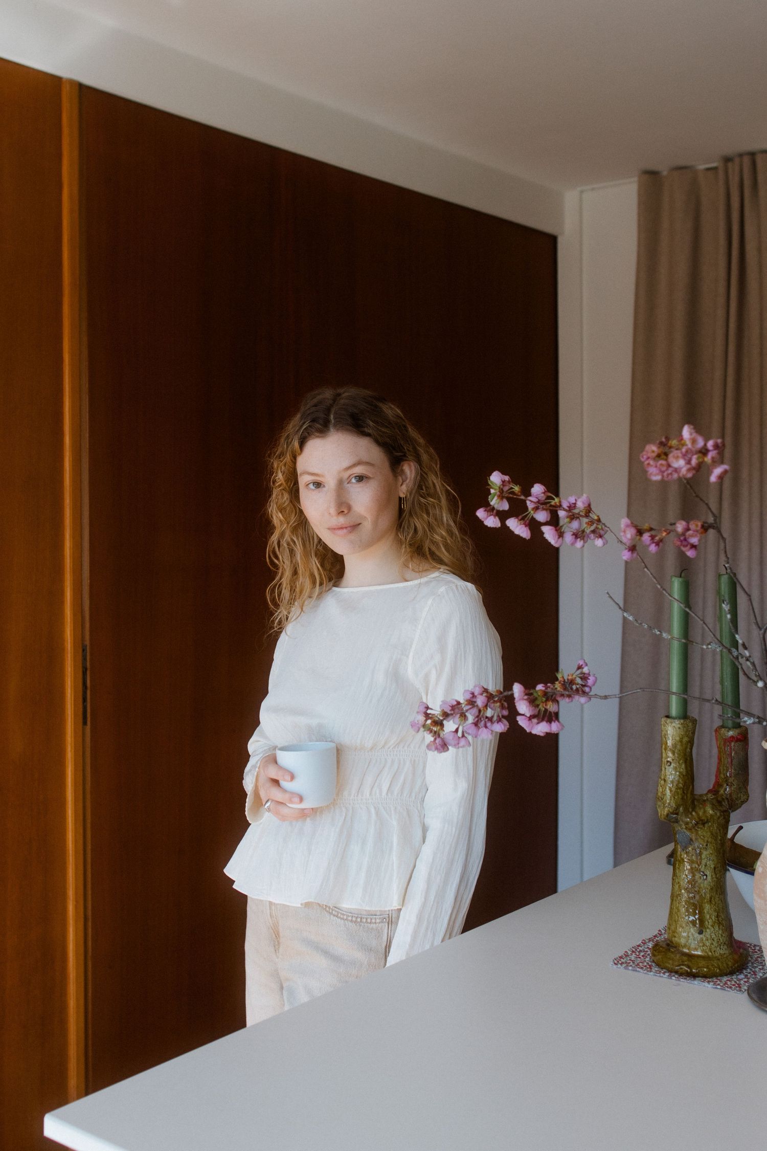 A person in a white blouse stands by a vase of pink orchids in a modern interior setting with warm wood paneling.